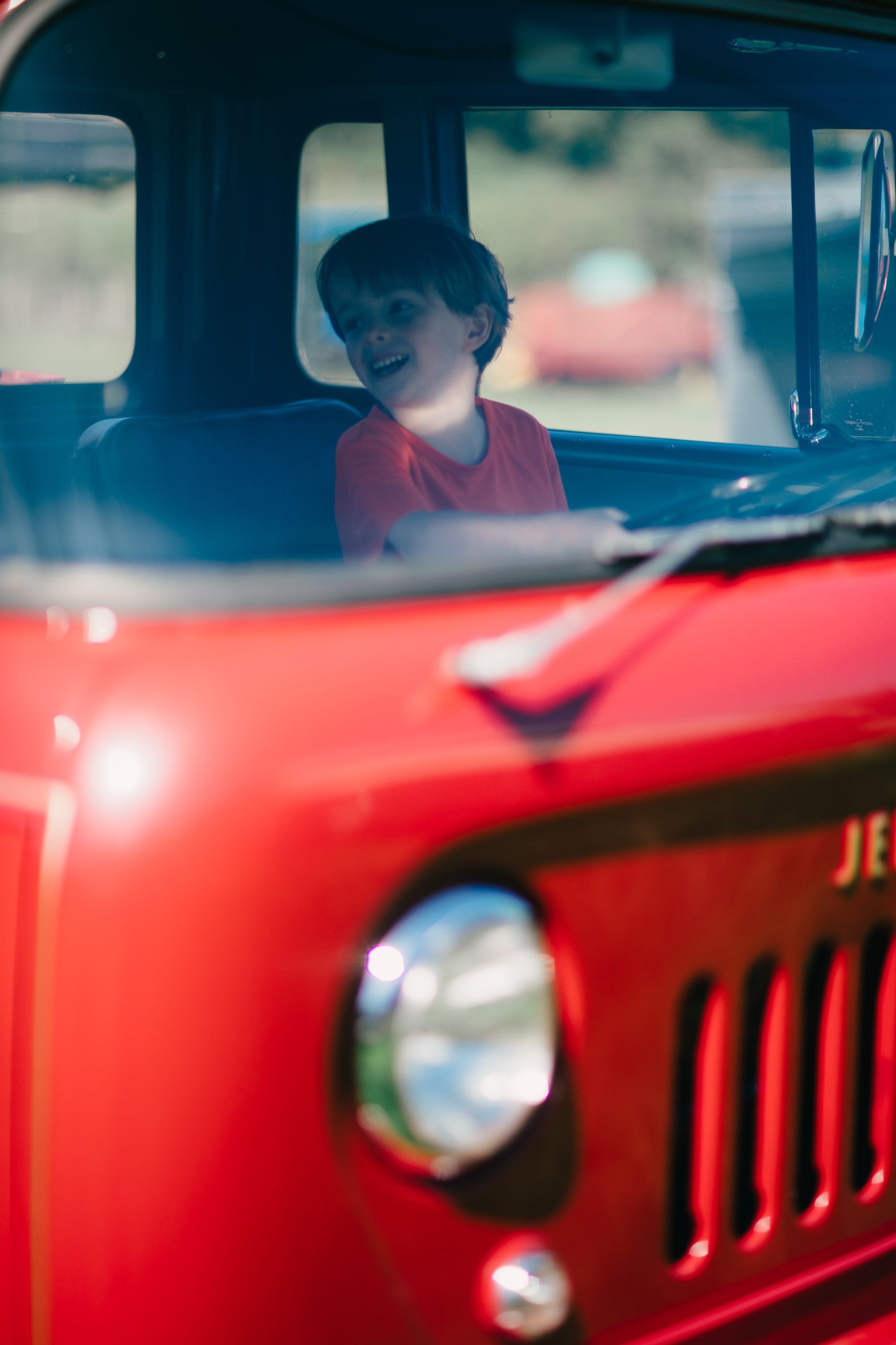 Child gazes through windshield of vintage red farm truck, soft light catching thoughtful expression