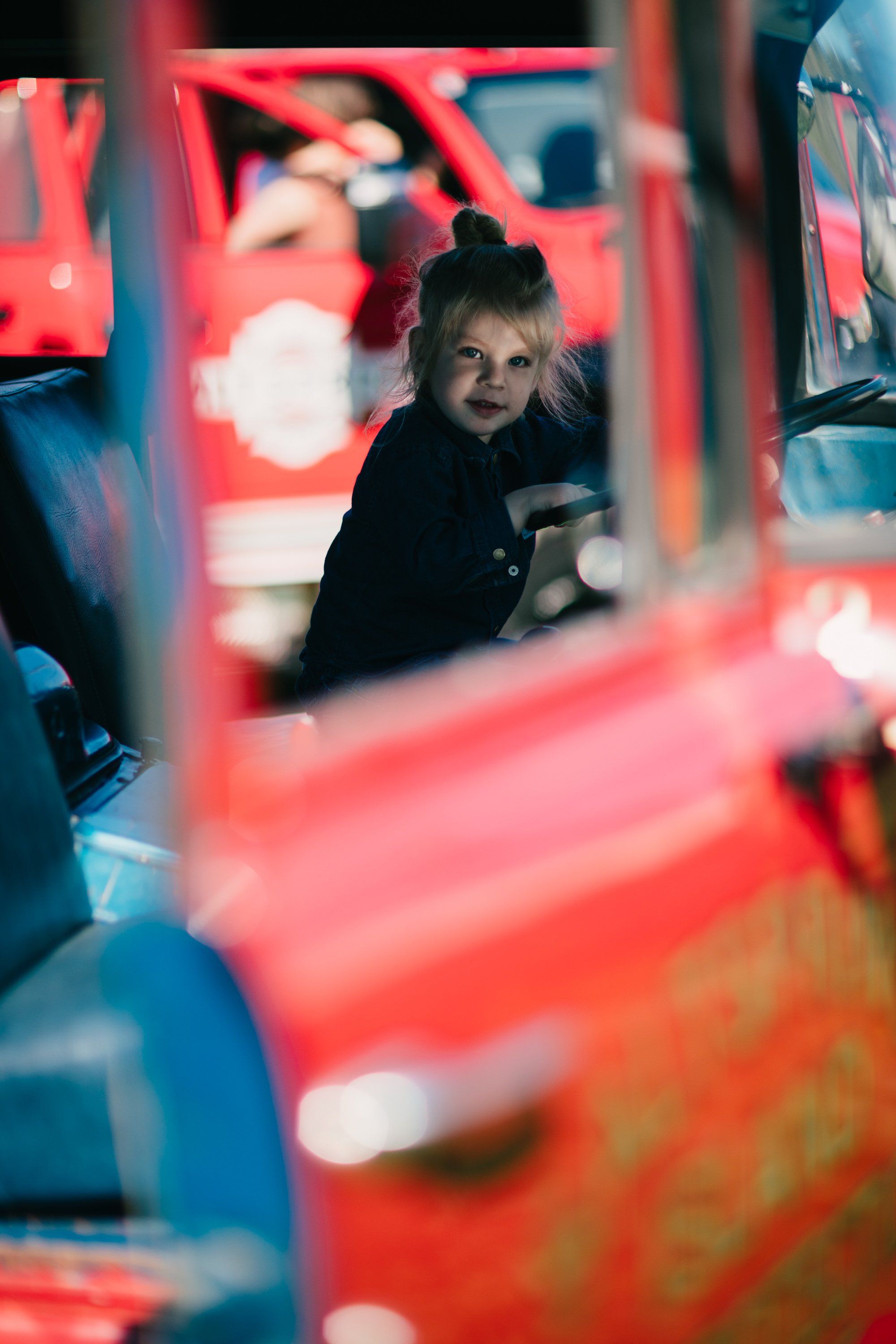 Child gazing through red carnival ride framework with warm bokeh lights at dusk