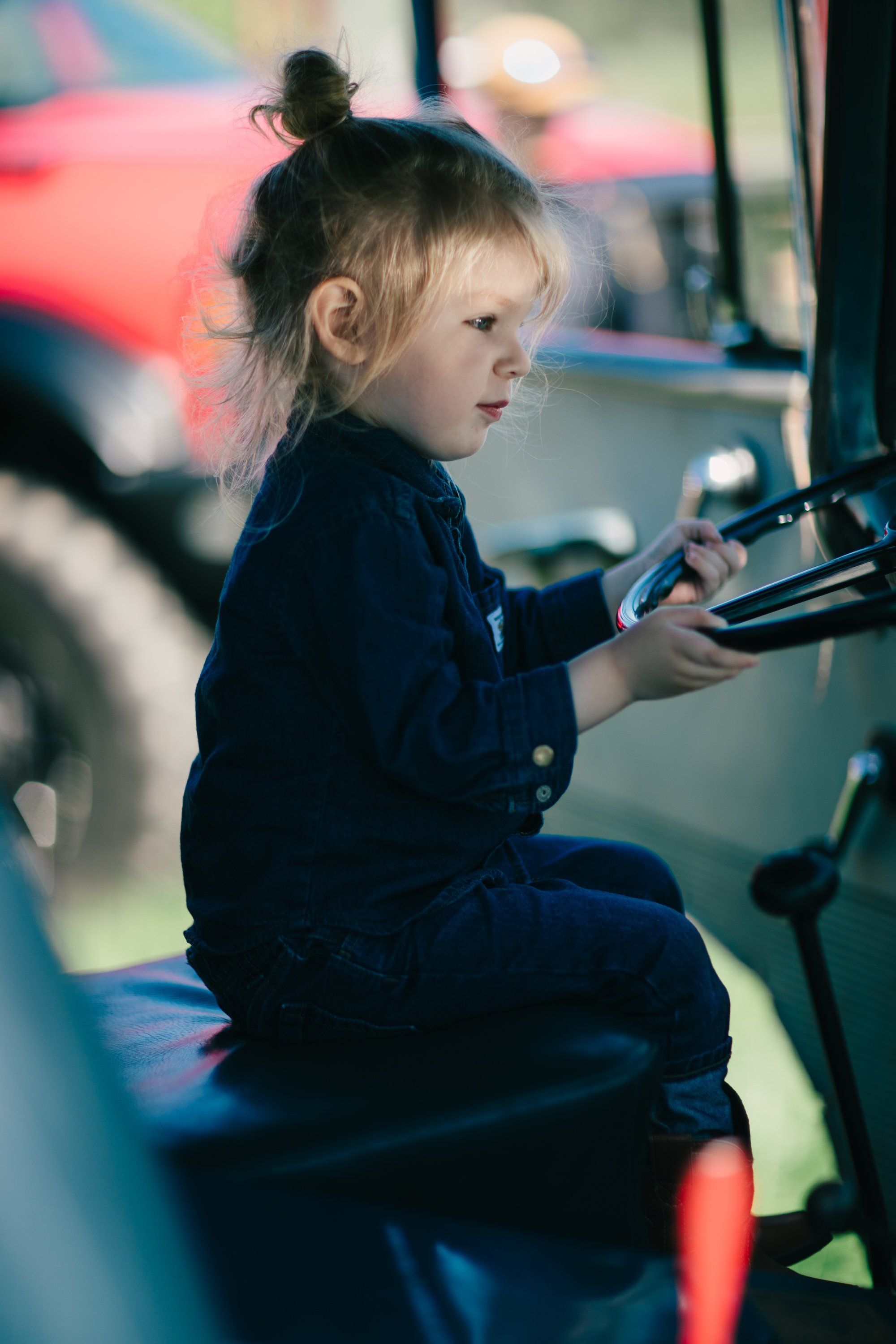 Young child in dark jacket sits at arcade game, bathed in warm and cool neon light, focused on controller