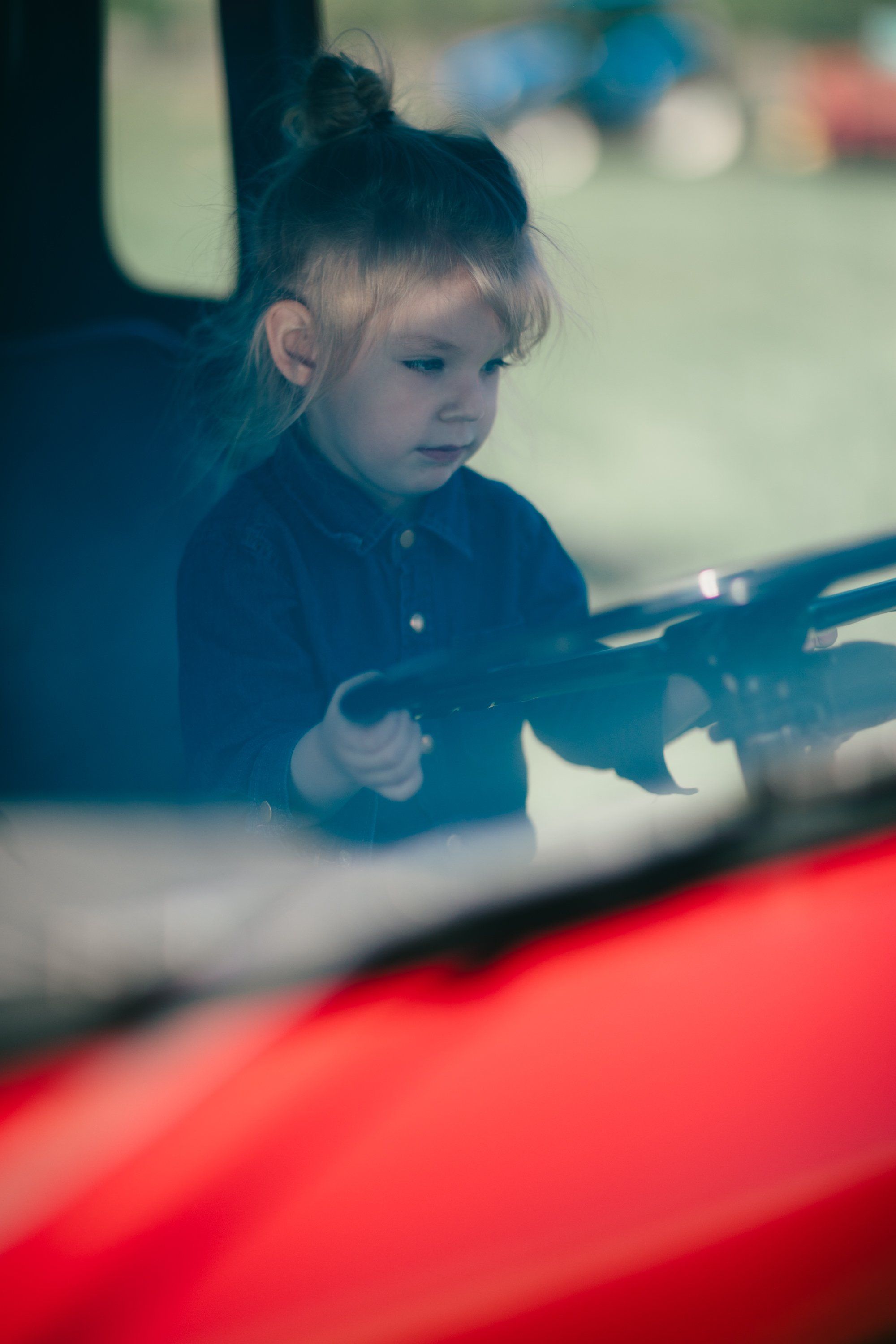Young child in dark shirt leans against weathered wooden farm equipment, soft natural light casting gentle shadows across contemplative expression
