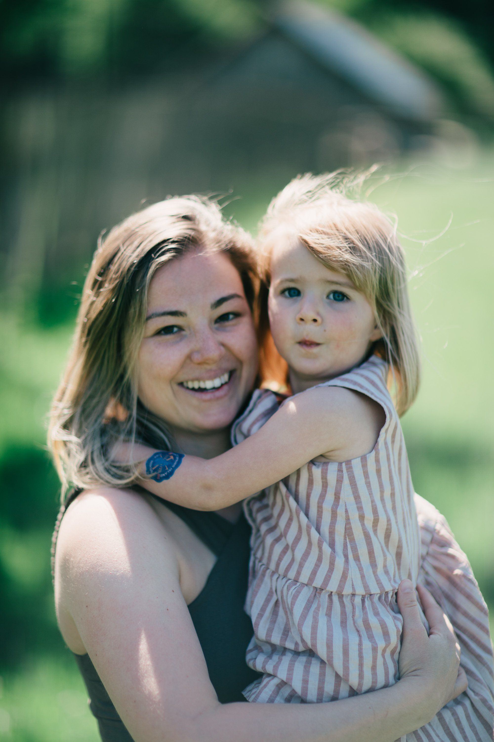 Woman holding young child outdoors at Ruckle Farm, both smiling at camera in warm afternoon light
