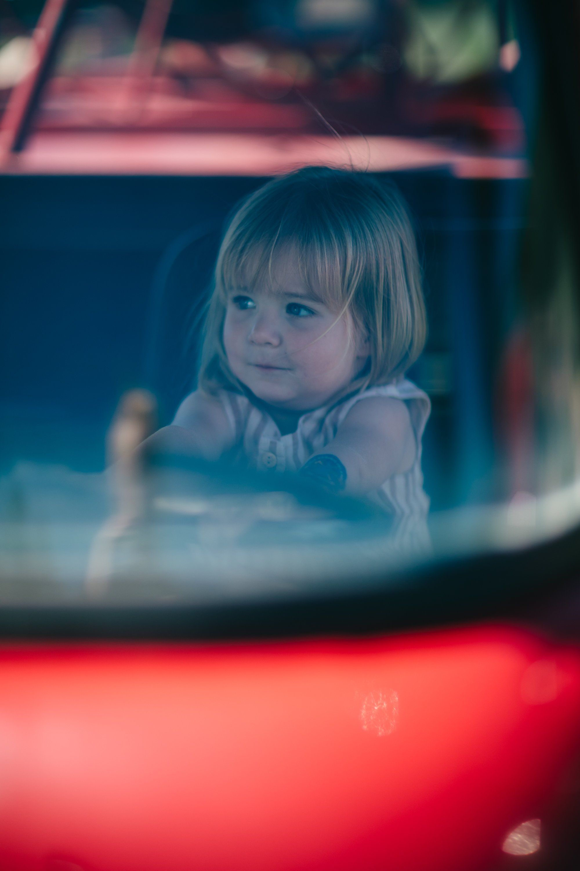 Toddler with blonde bob gazing thoughtfully amid warm red and cool blue neon light, soft focus farmstead backdrop