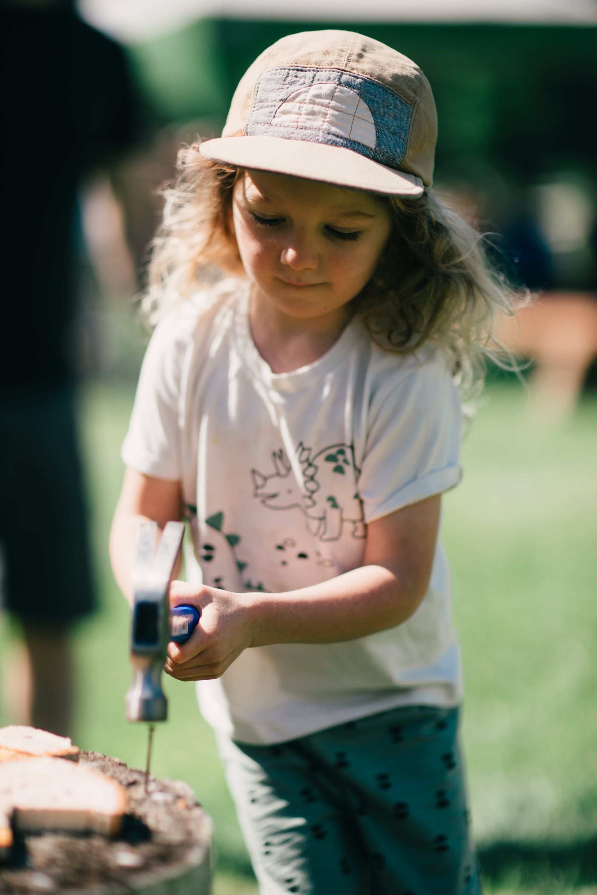 Young girl in cap and white shirt uses a garden tool in sunlit farm field, focused on her work