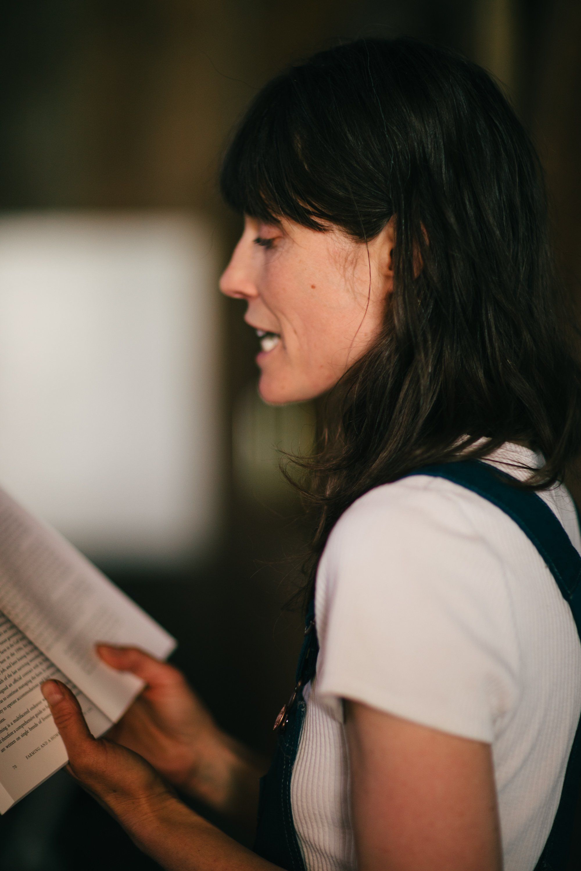 Woman in white t-shirt holding papers, smiling in profile against soft, blurred background light