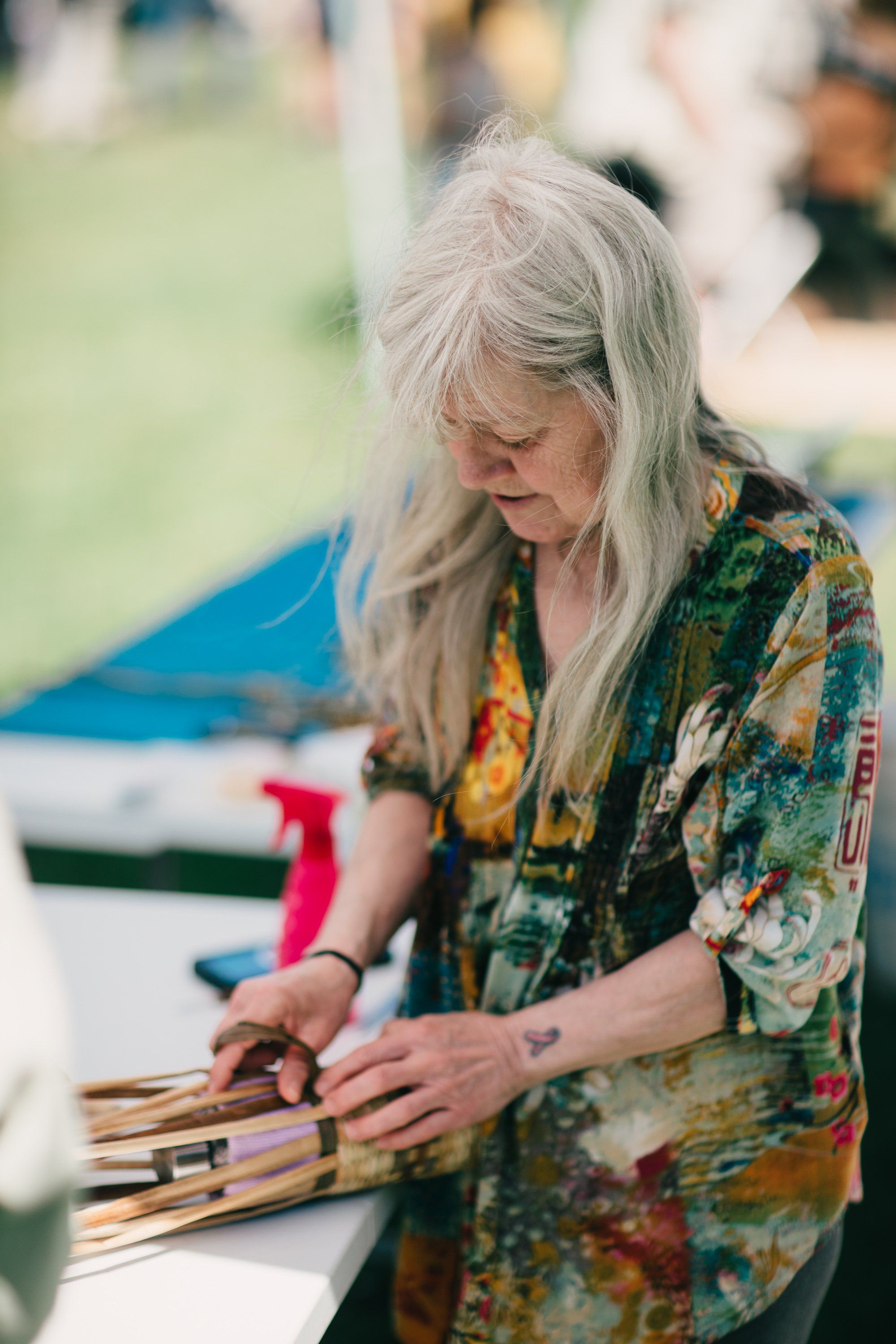Woman with long gray hair in floral shirt weaves dried grass at Ruckle Farm, soft daylight filtering through