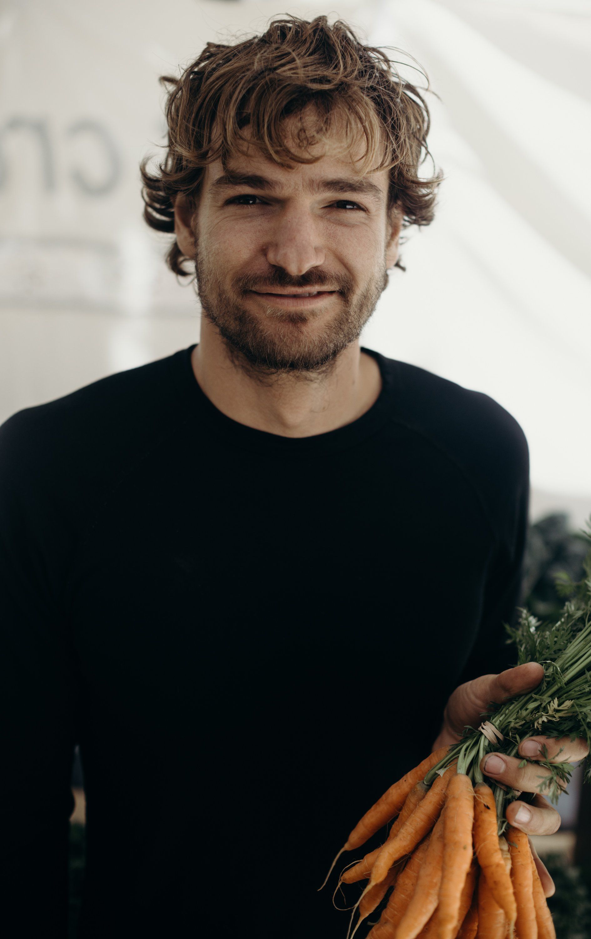 Man with tousled blonde-brown hair and full beard smiles warmly at Salt Spring Island Tuesday Farmers Market