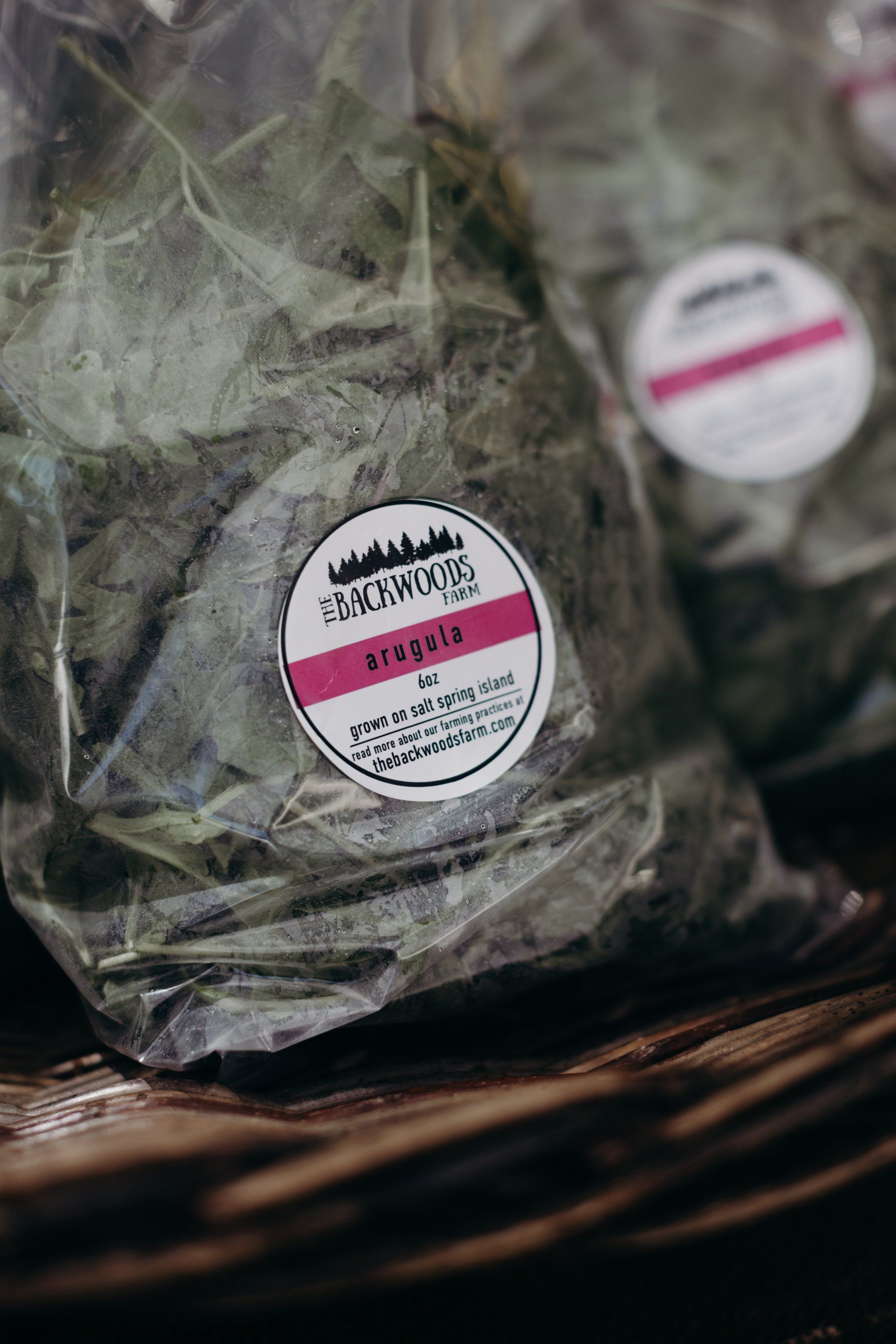 Packaged herbs with pink-striped labels rest on weathered wood at the farmers market, soft natural light illuminating the fresh produce display
