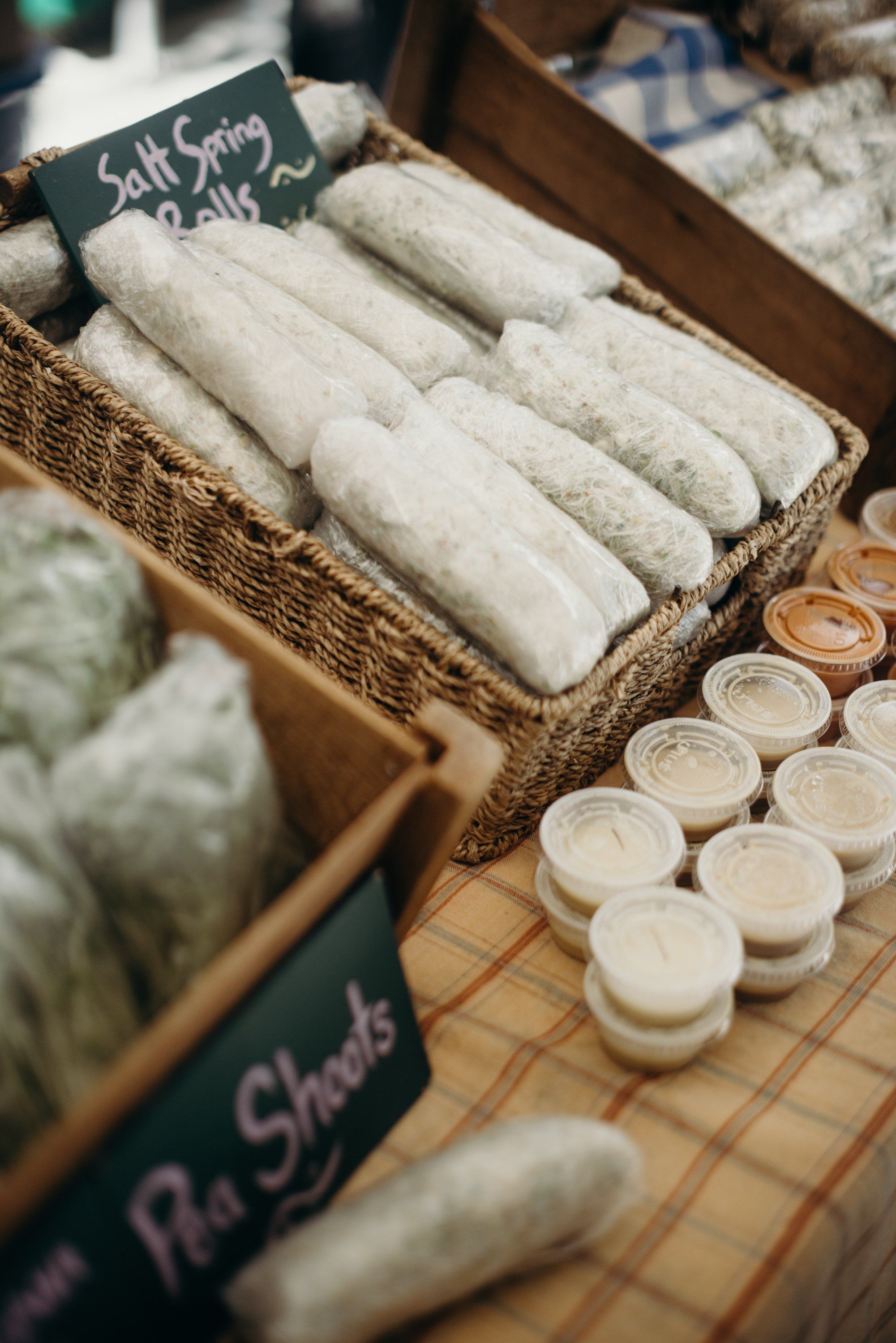 Woven basket of rolled white linens with handwritten "Salt Soap" sign at farmer's market, small glass jars beside
