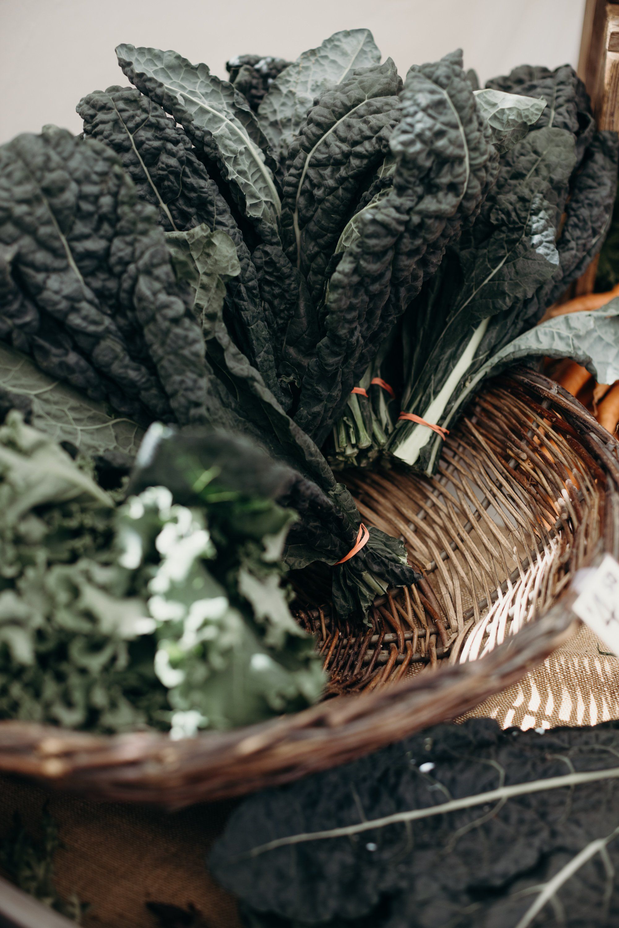 Deep green leafy vegetables with textured ridged leaves bundled at a farmer's market stand, showing fresh produce detail and natural morning light