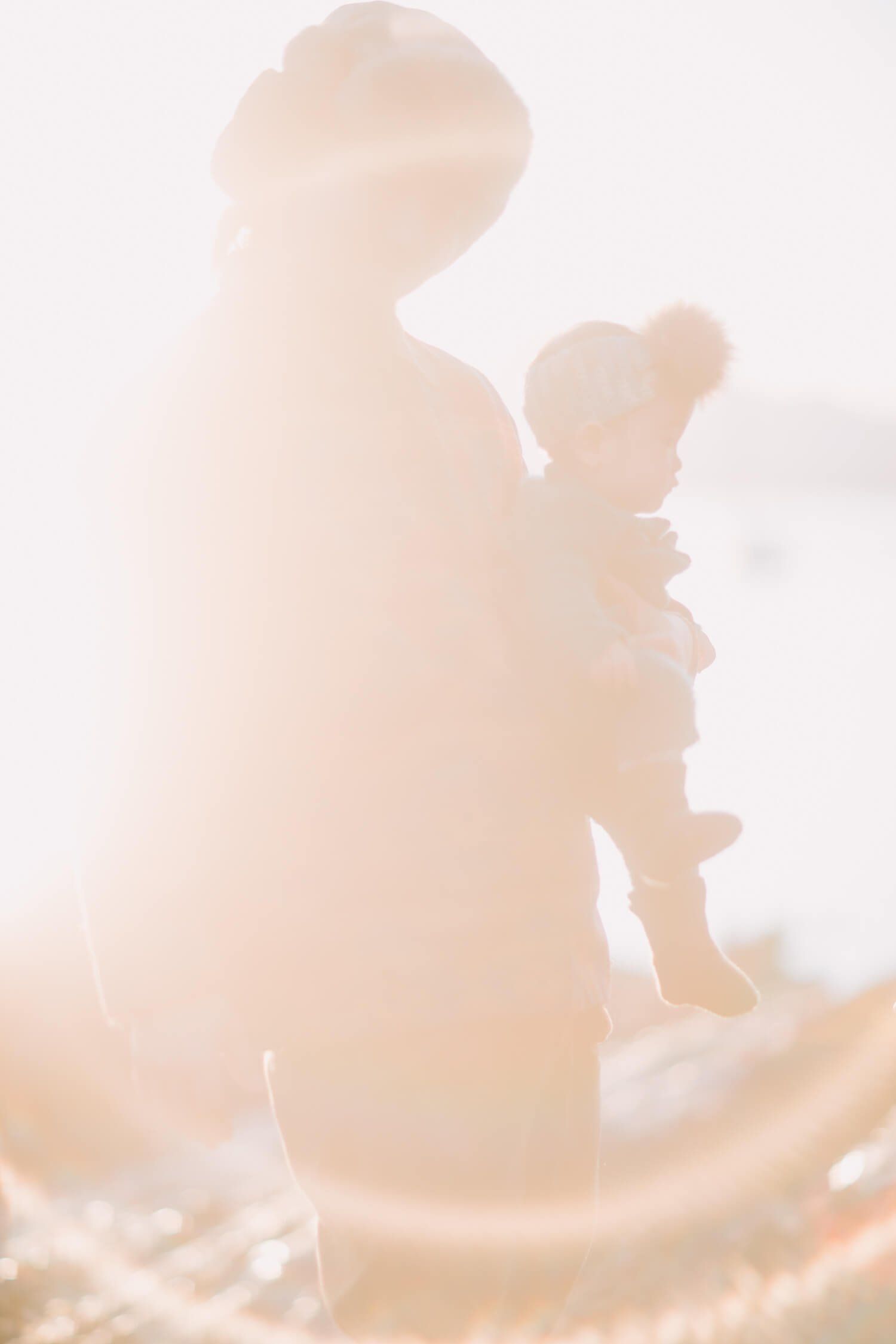 Silhouetted parent holding small child against bright, overexposed window light creating a soft, dreamy golden glow