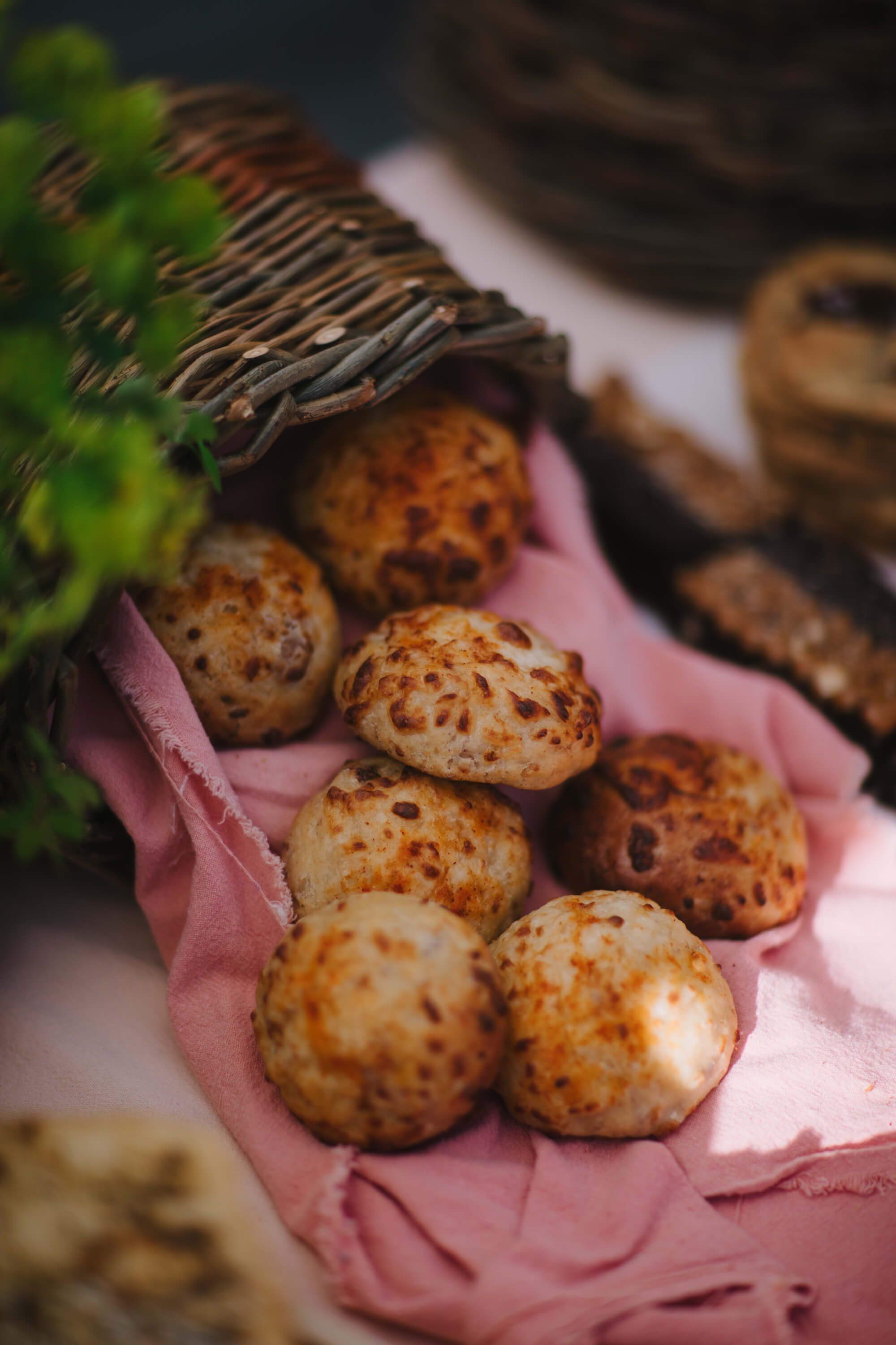 Golden-brown pastries nestled in pink tissue paper at a farmers market stall, with woven baskets and fresh greens visible above