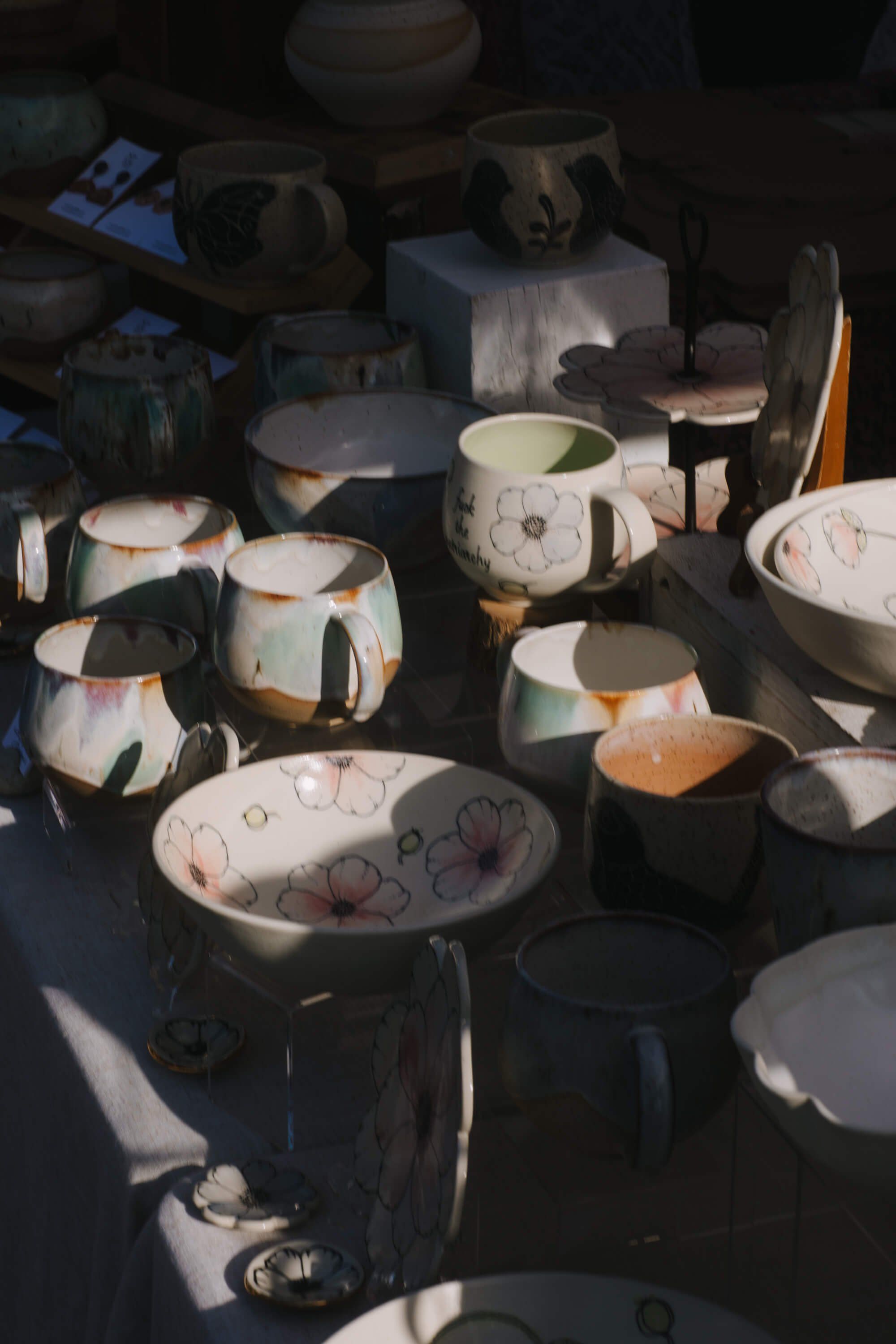 Handmade ceramic vessels with organic glazes and warm earth tones displayed on dark surfaces, lit by natural sunlight at an outdoor market
