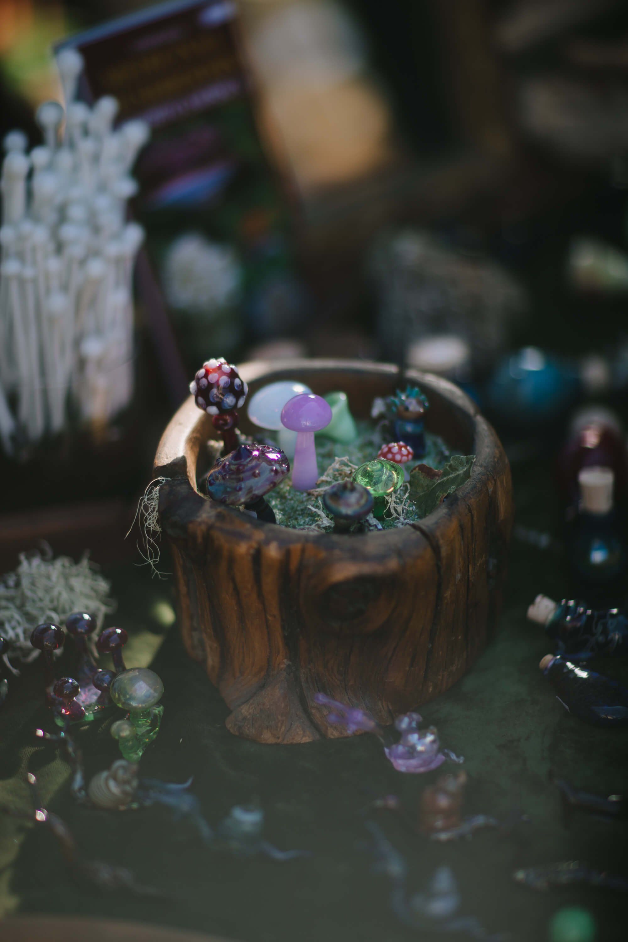 Wooden bowl filled with miniature succulents and moss figurines, softly lit with bokeh crystals glowing in warm and cool tones behind it