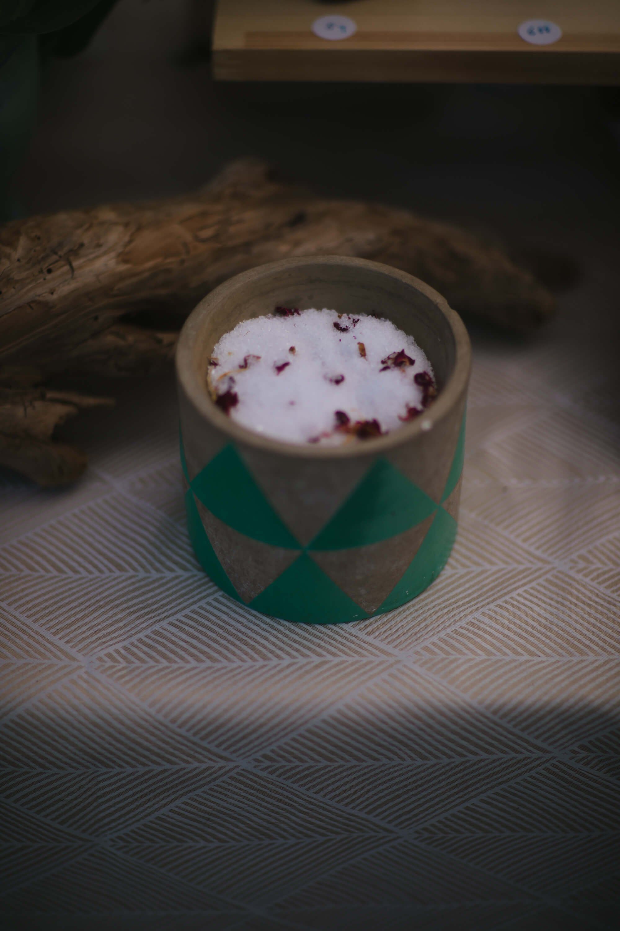 Creamy cappuccino topped with cocoa powder in a geometric green and grey cup beside driftwood at the market