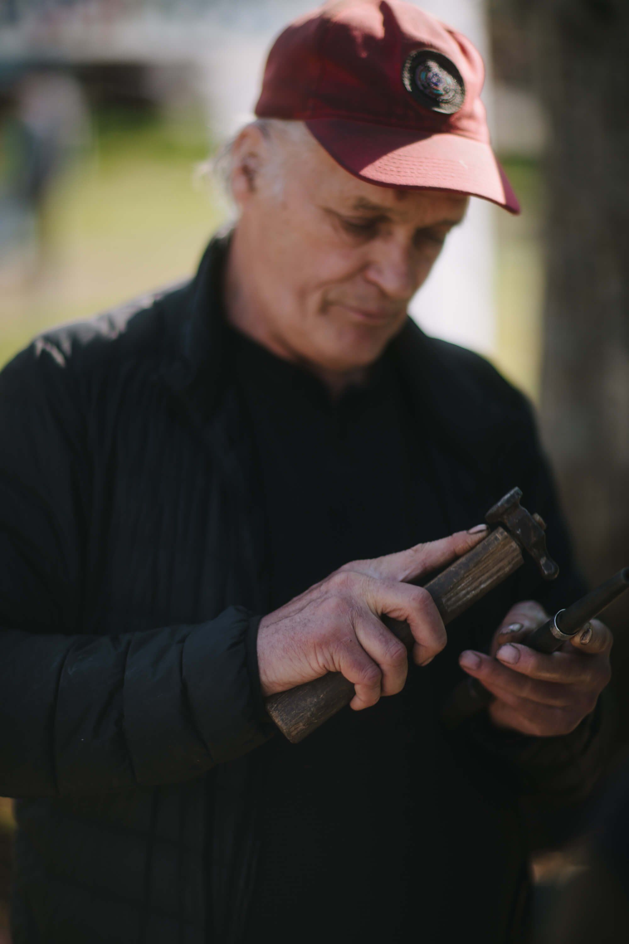 Man in maroon cap examining camera in soft outdoor light at market setting