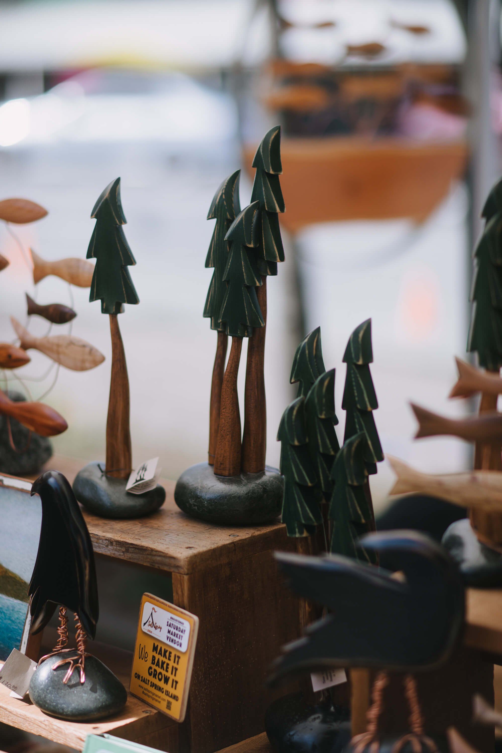 Handcrafted wooden tree figurines with dark green fabric foliage displayed at an outdoor market stall