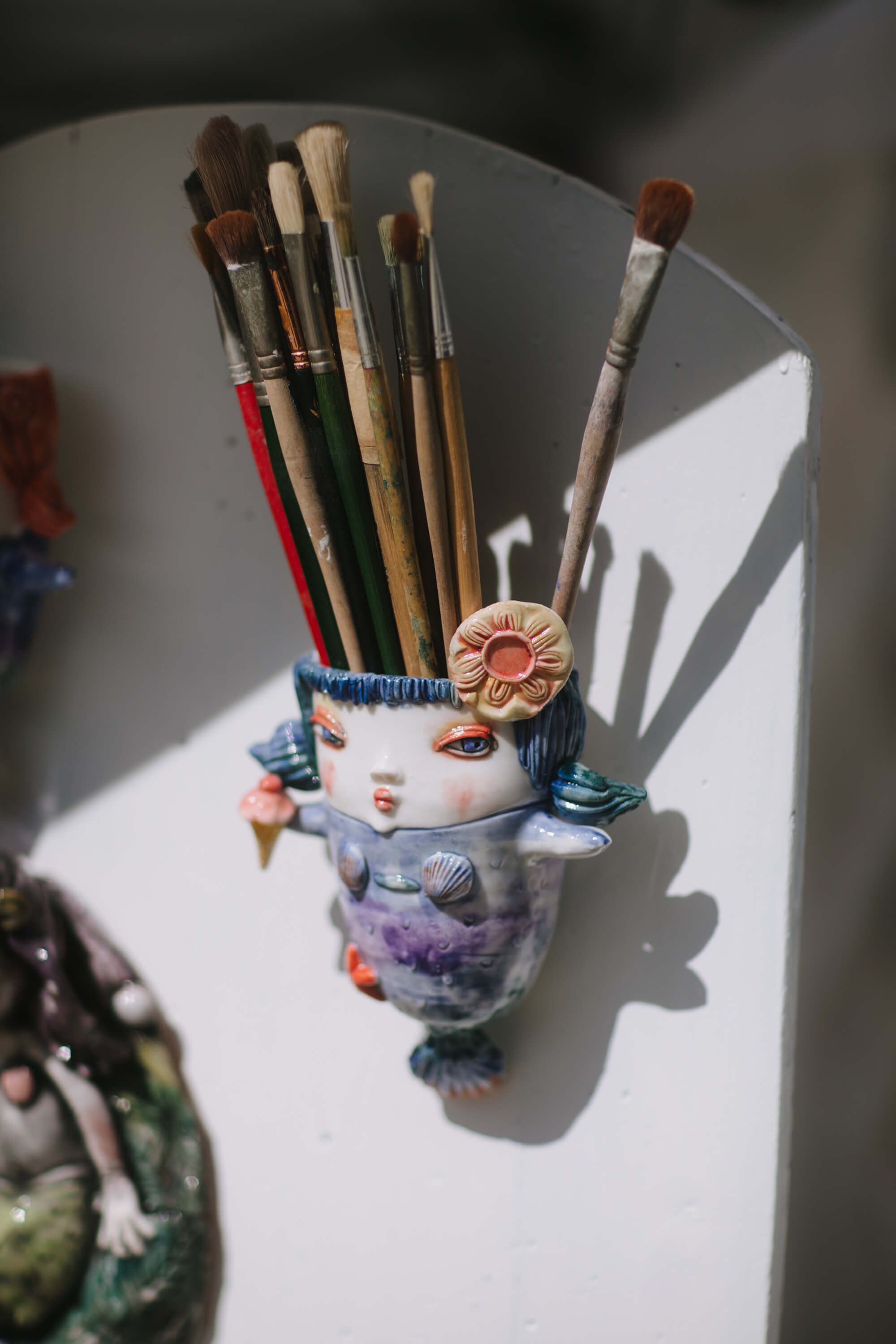 Paintbrushes in a decorative ceramic holder casting shadows in bright sunlight at an outdoor market
