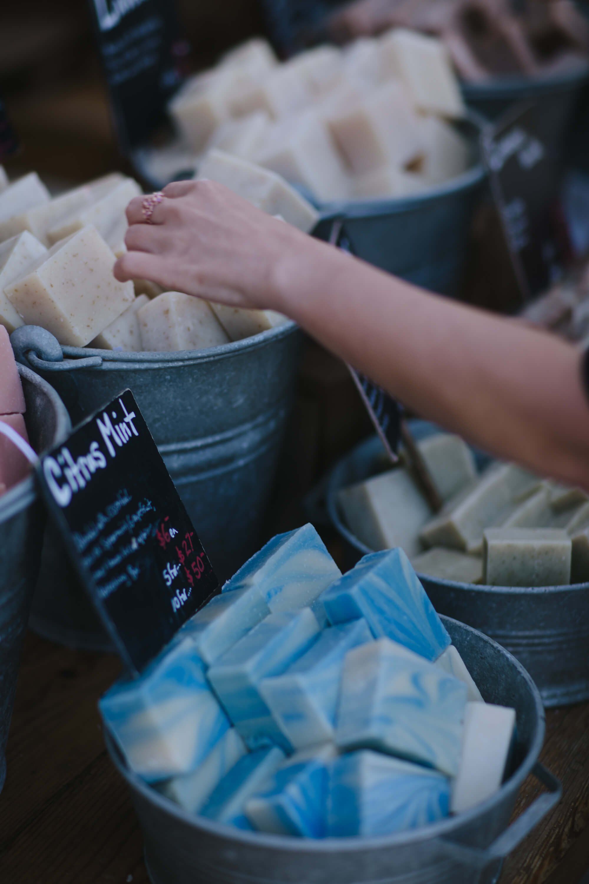 Child's hand reaching into a bucket of fresh tofu at an outdoor market stall on a bright day