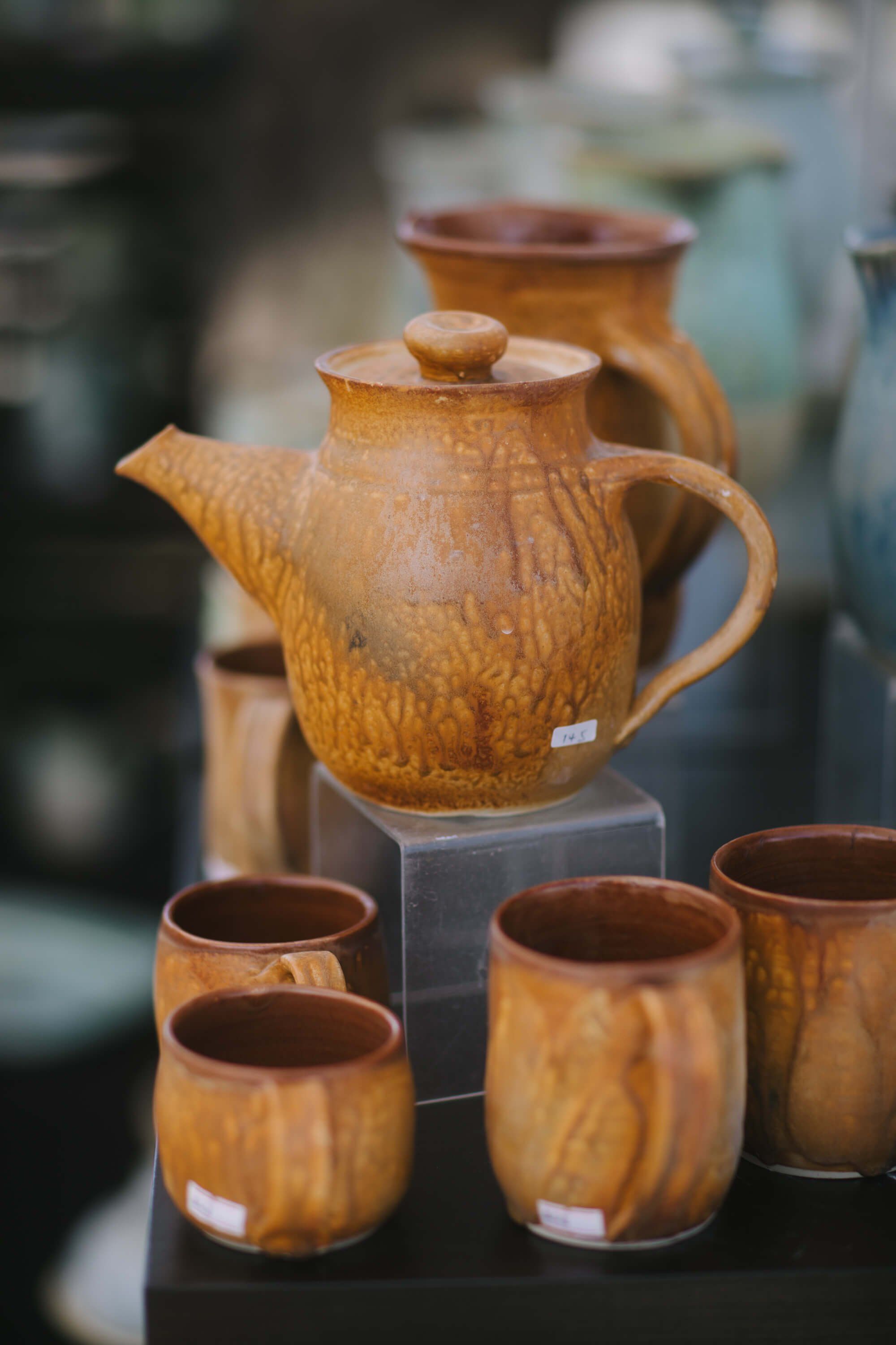 Handcrafted wooden teapot and matching cups displayed at a market stall, warm amber wood grain catching natural light