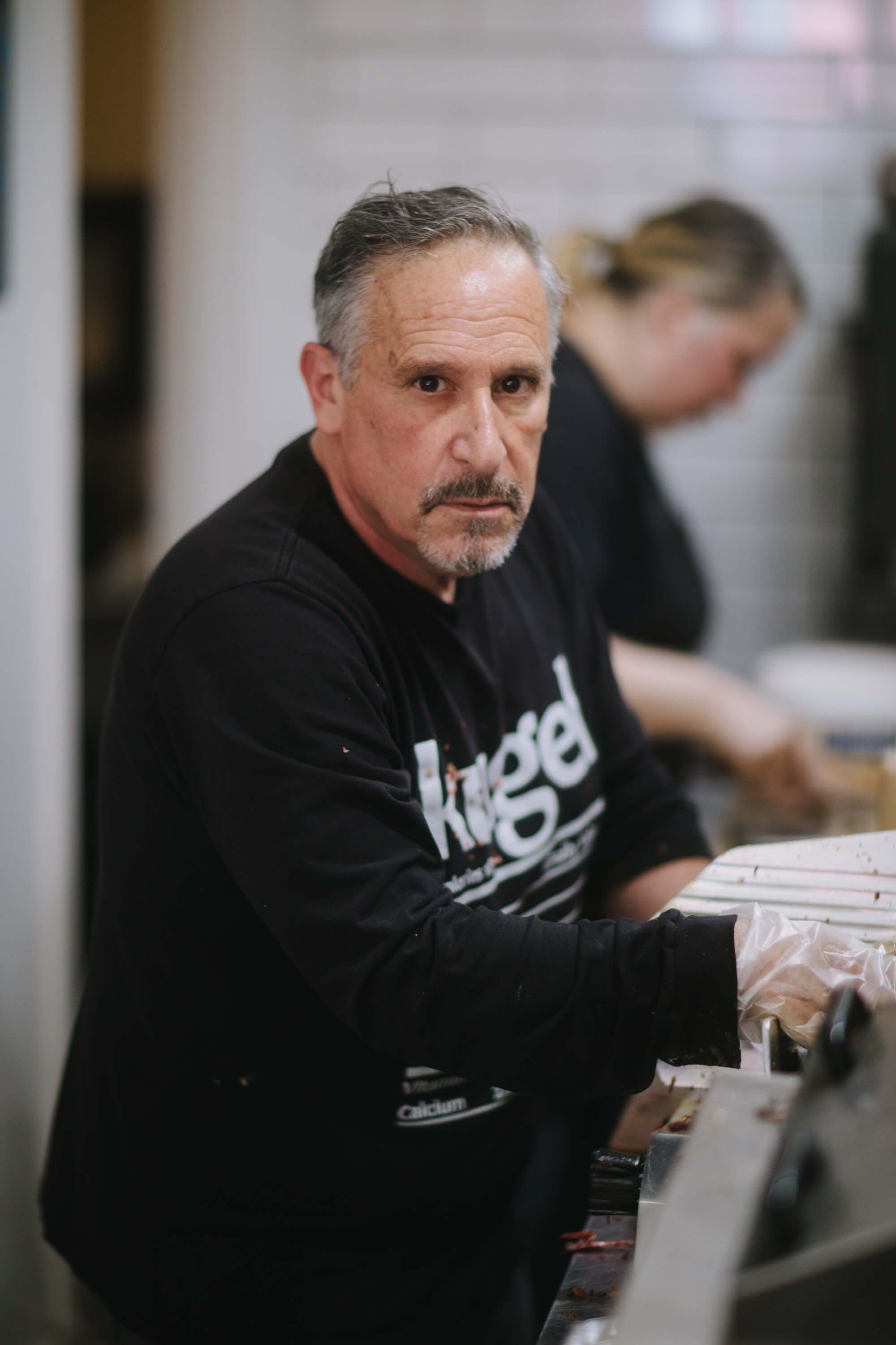 Man in black shirt examining items at market table, focused expression, soft indoor lighting