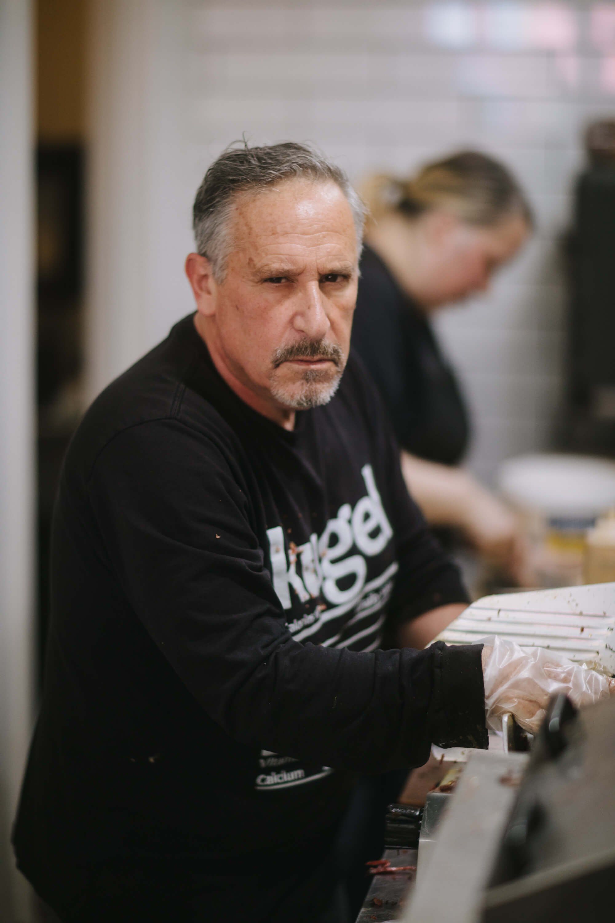 Man in black shirt holding papers at indoor market table, focused expression, blurred activity in background
