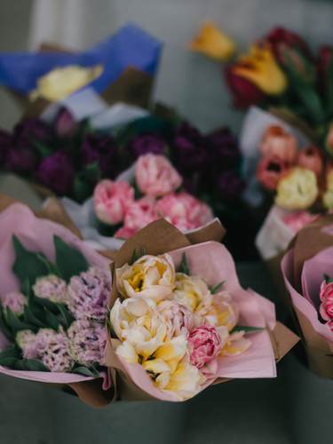 Delicate peony bouquets wrapped in soft pink paper with layered cream and pink blooms displayed at a flower vendor stall
