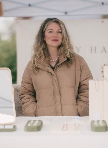 Woman in tan puffer jacket smiling at Saturday Market under white tent canopy