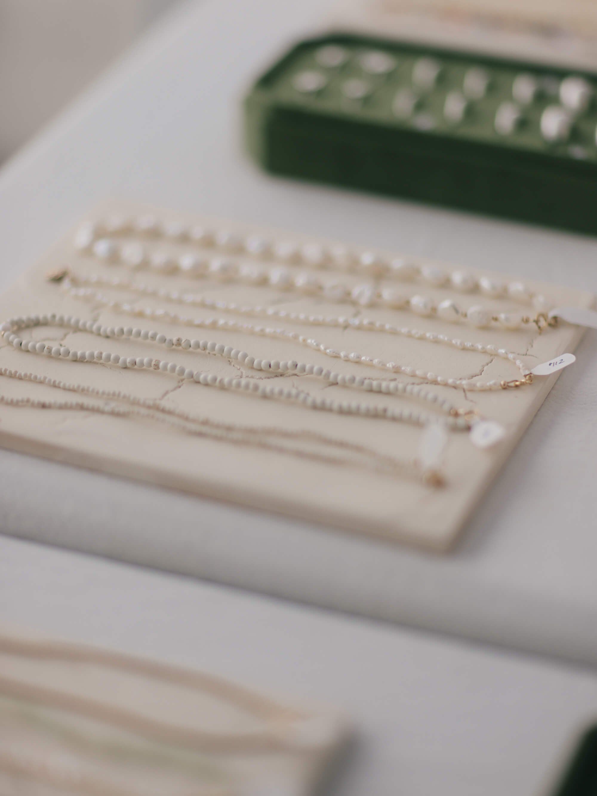 Delicate pearl necklaces draped on cream display stands at an outdoor market vendor booth