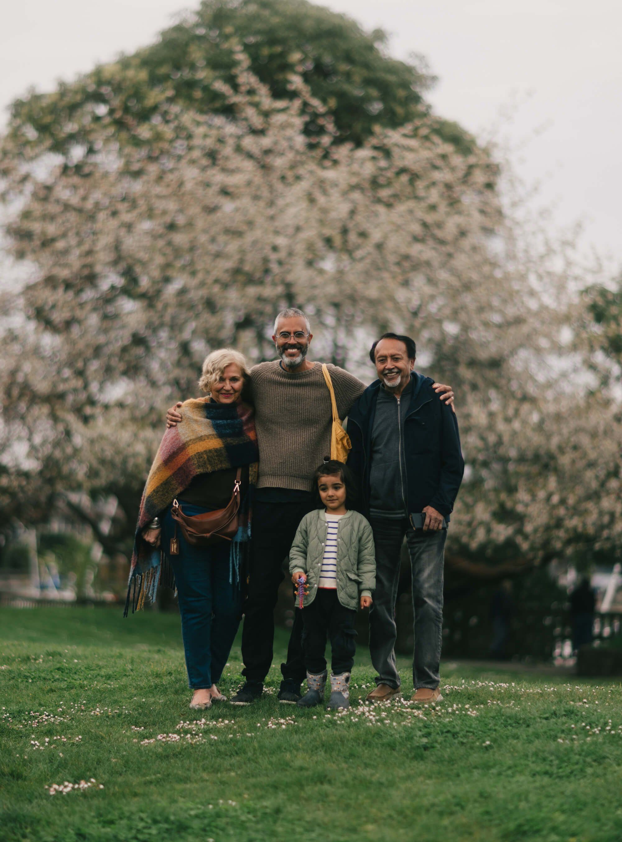 Four-generation family portrait on grass with massive flowering tree in soft, overcast light