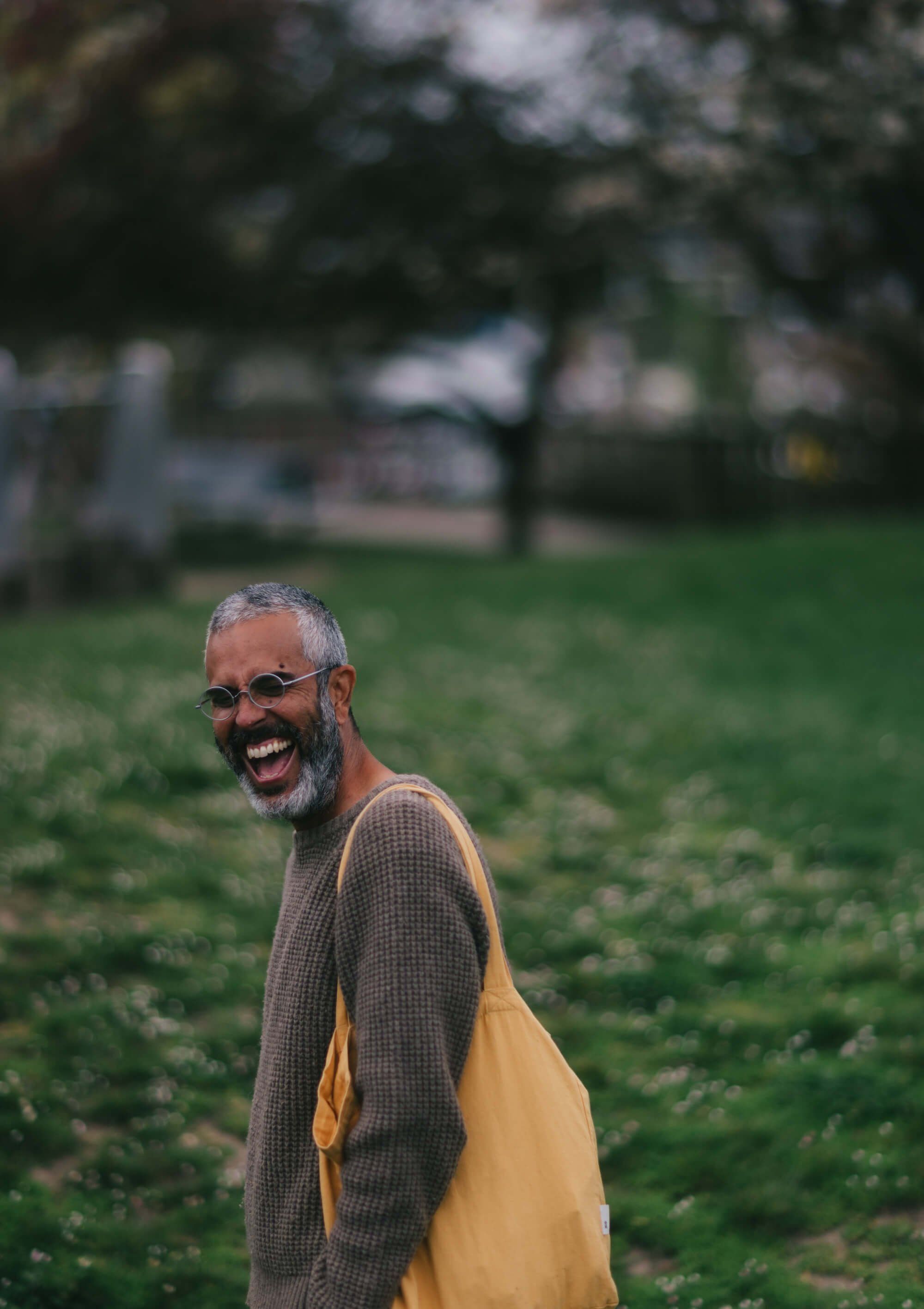 Bearded man in glasses and yellow shirt smiling at camera in sunlit park setting