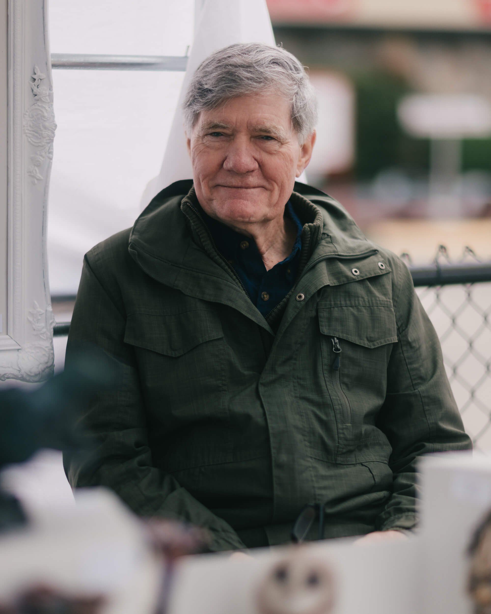 Gray-haired man in olive jacket smiles at Salt Spring Island Saturday Market, soft natural light