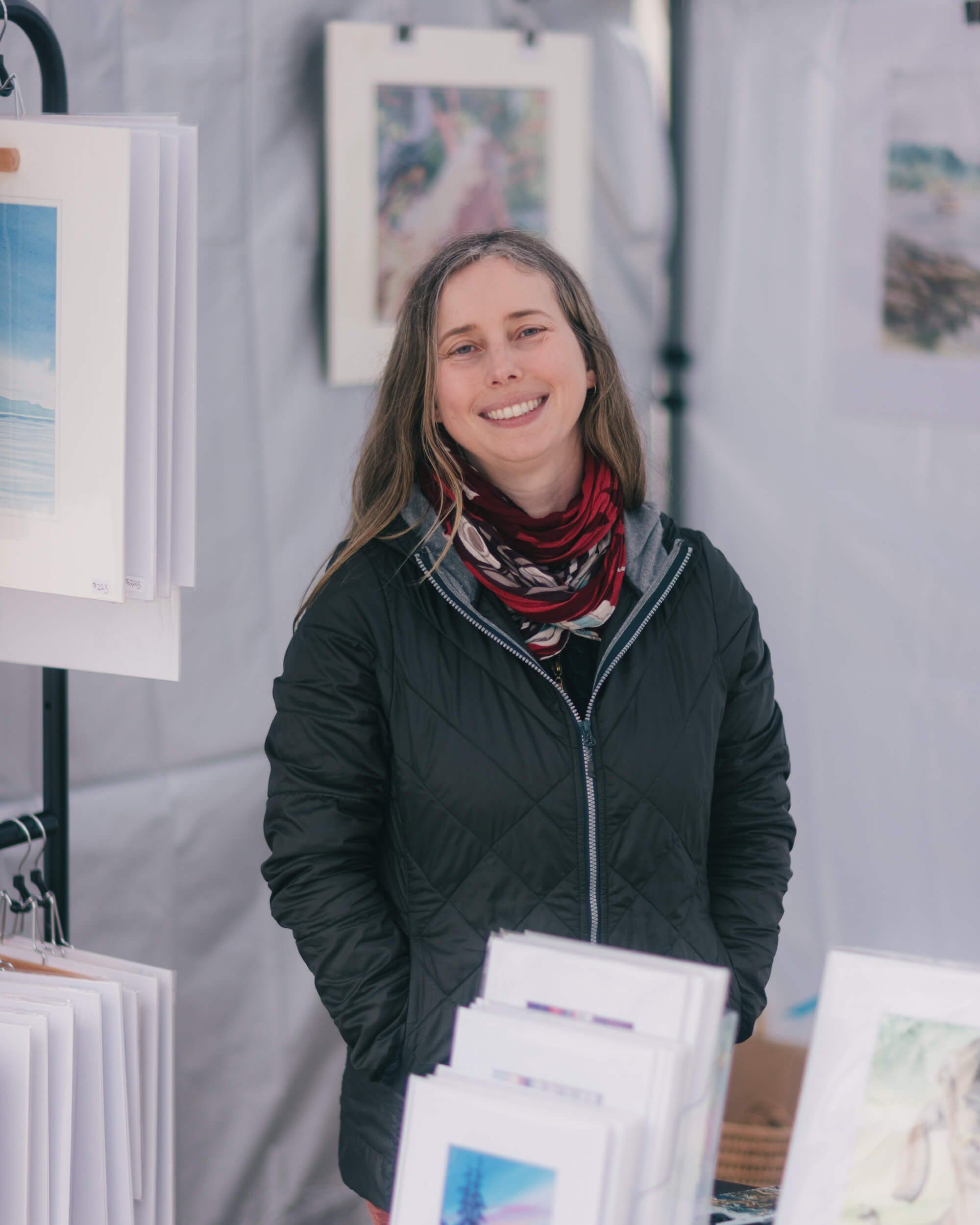Woman smiling at Saturday Market booth displaying fine-art prints and photographs on white walls