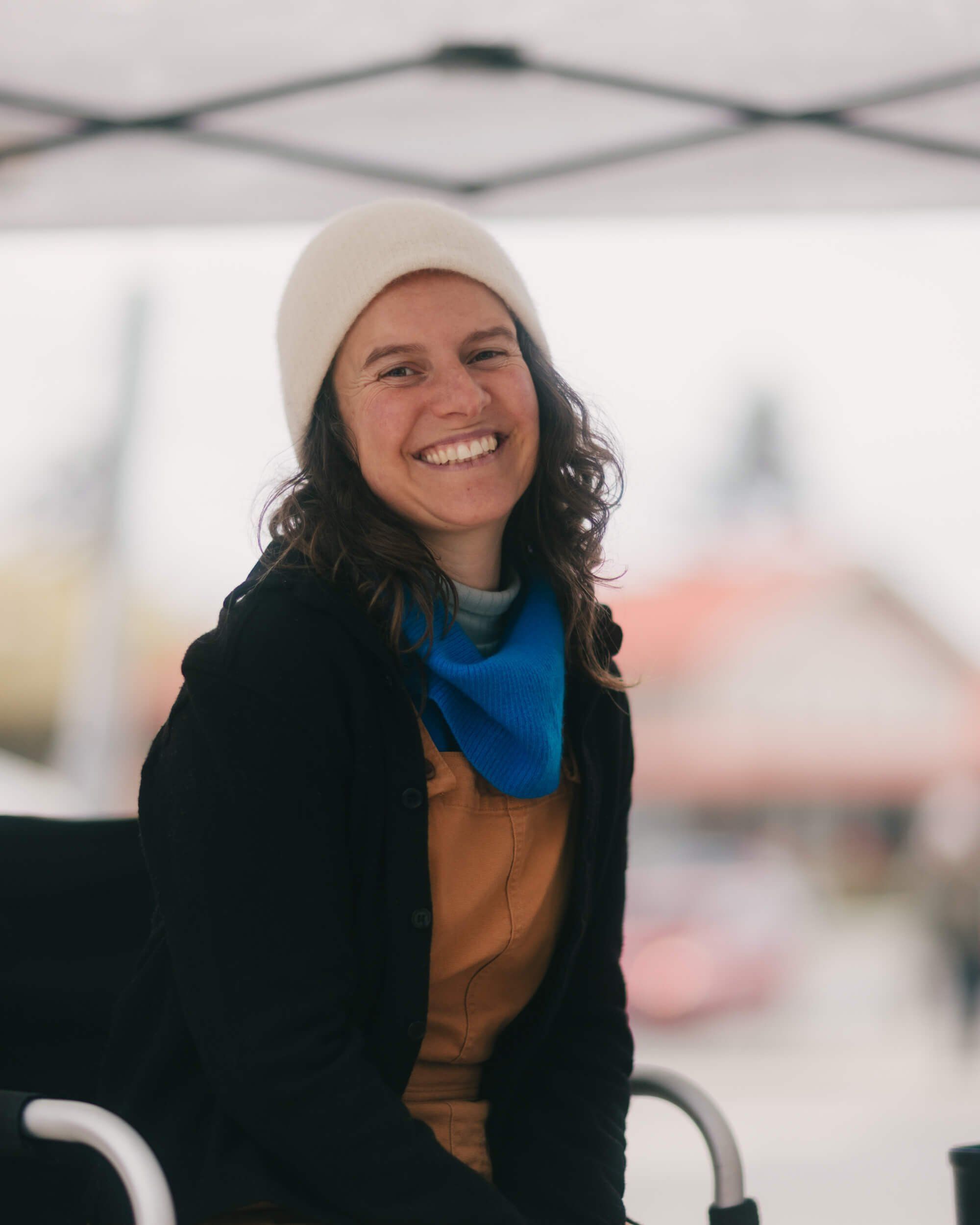 Smiling woman in cream beanie and black jacket at the Saturday Market, bright natural light