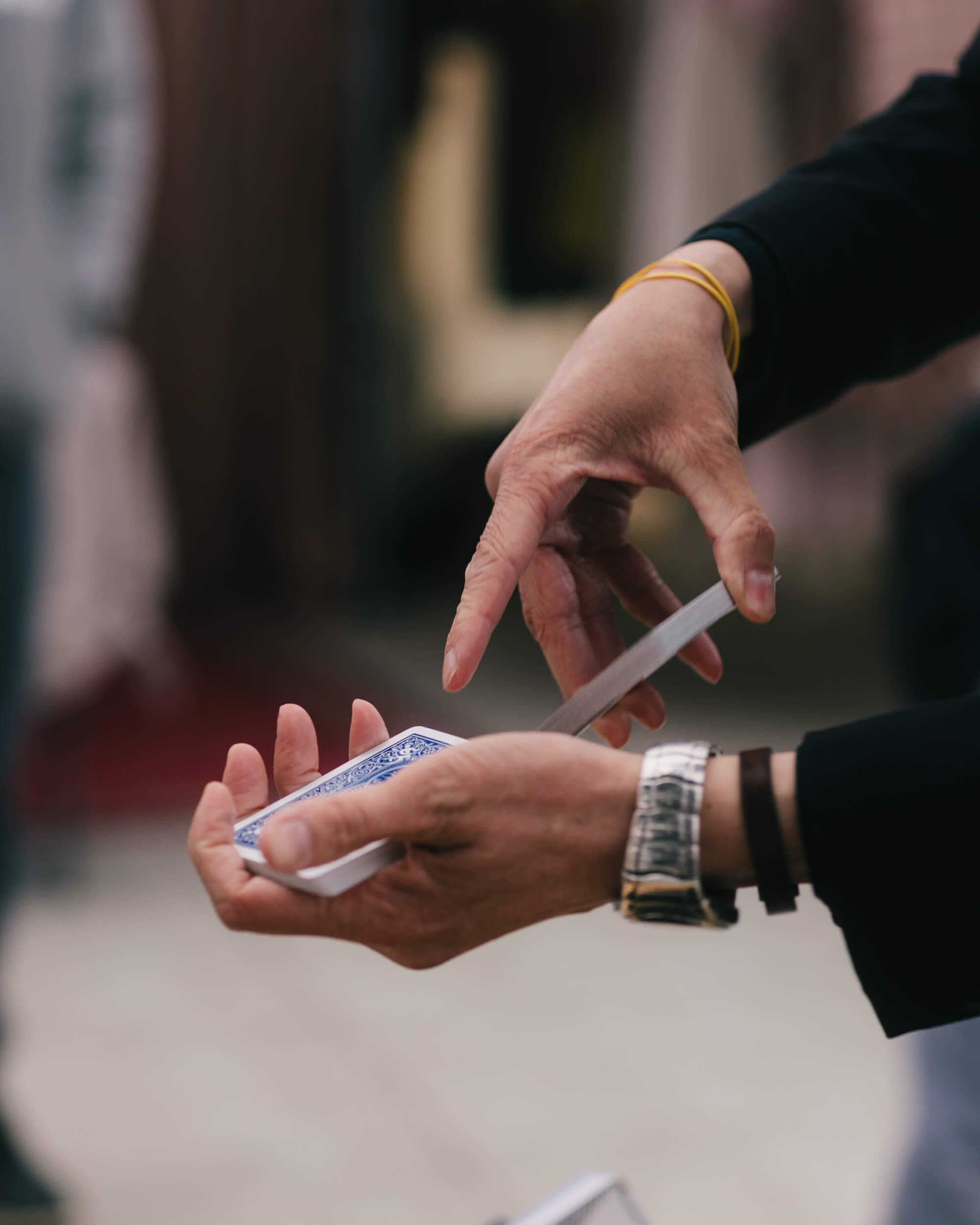 Two hands exchange a small white item at an outdoor market, with blurred figures and warm earth tones in the background