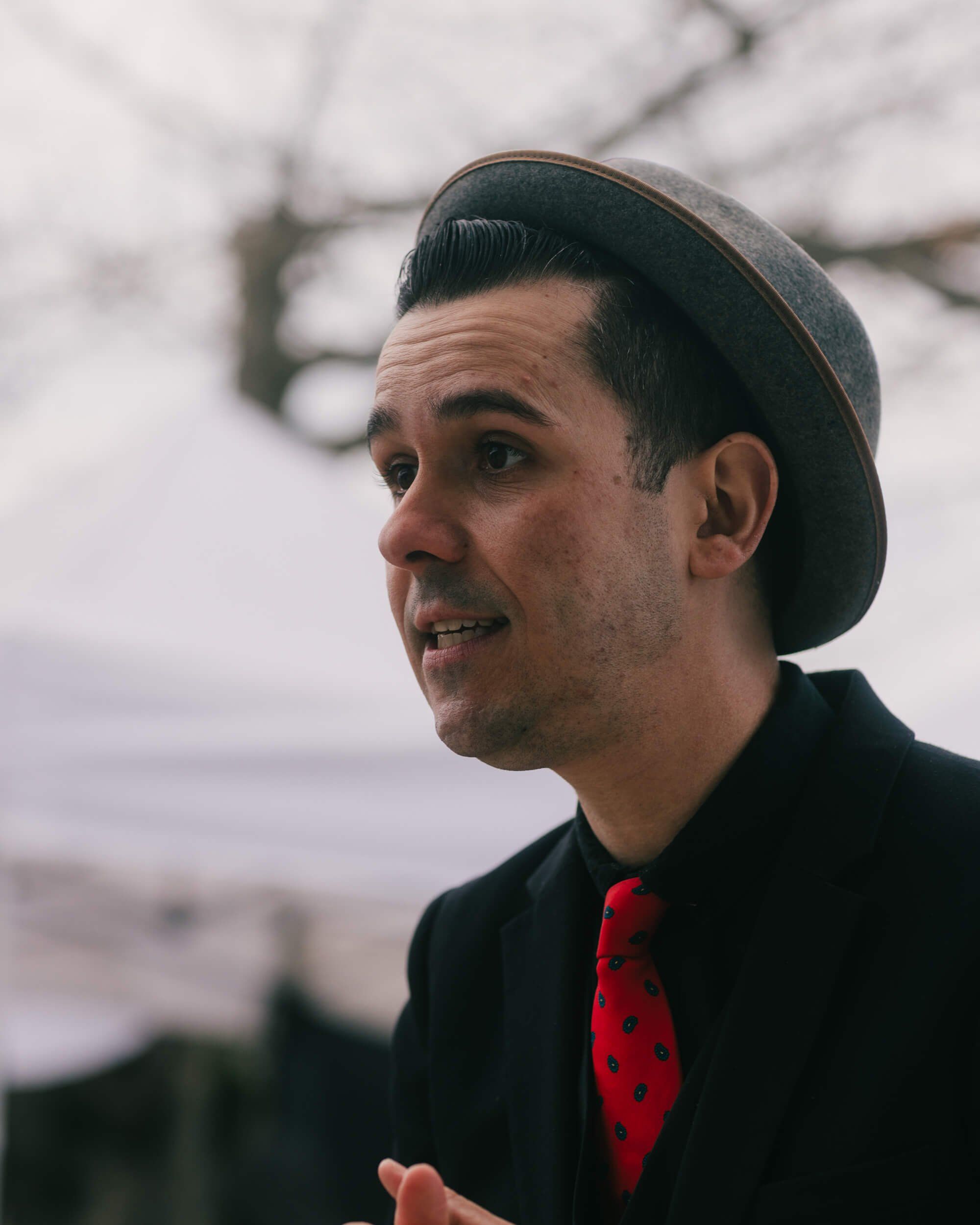 Man in dark coat and red tie smiles at Salt Spring Island market, overcast sky behind him