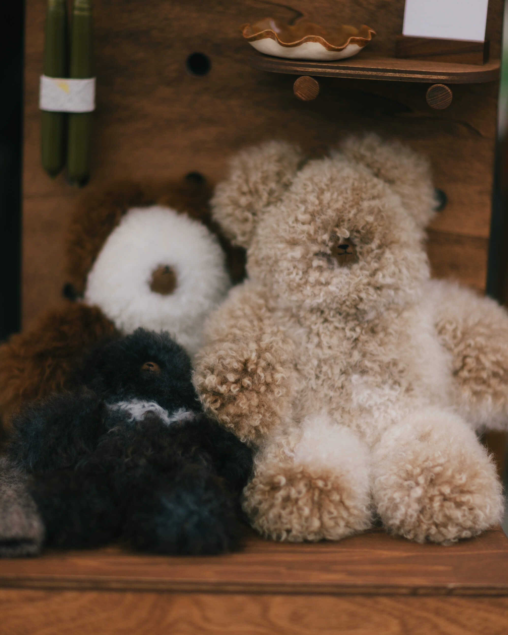 Three plush stuffed animals arranged on weathered wood shelf among vintage market items and warm afternoon light