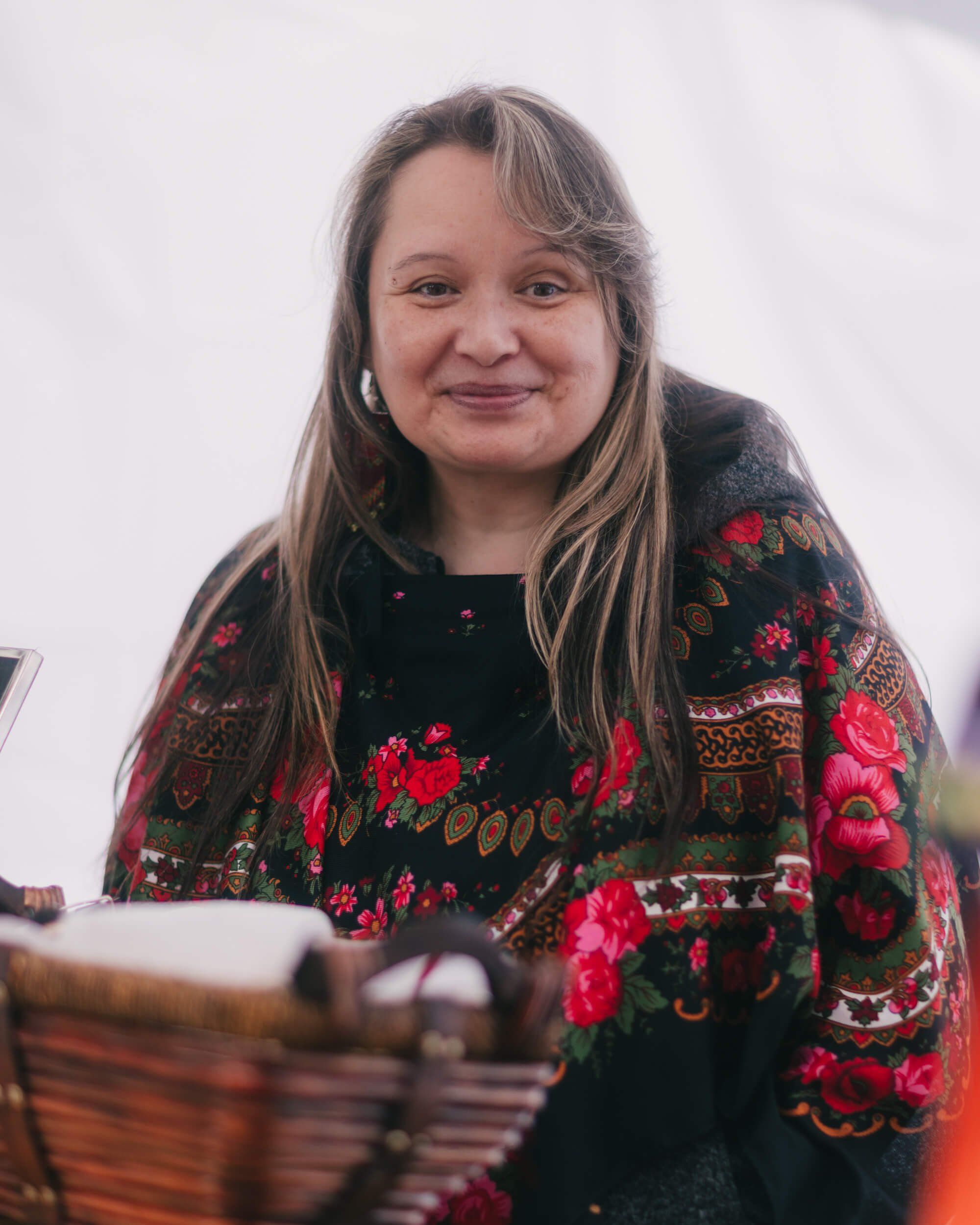 Woman in embroidered black cardigan with red floral details smiles warmly at Saturday Market, soft natural light