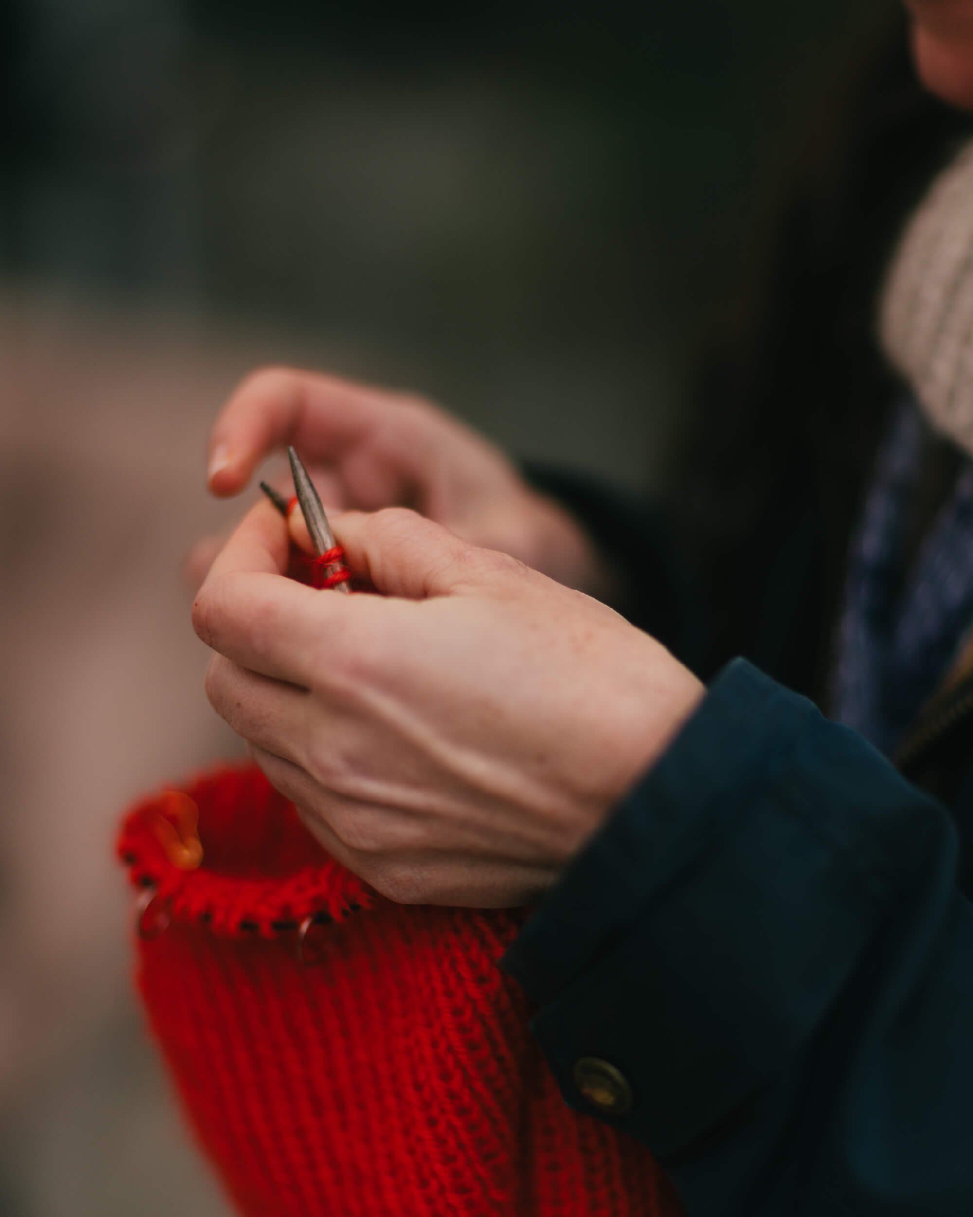 Hands holding a red berry with soft natural light, wearing dark sleeve and red knit fabric at market