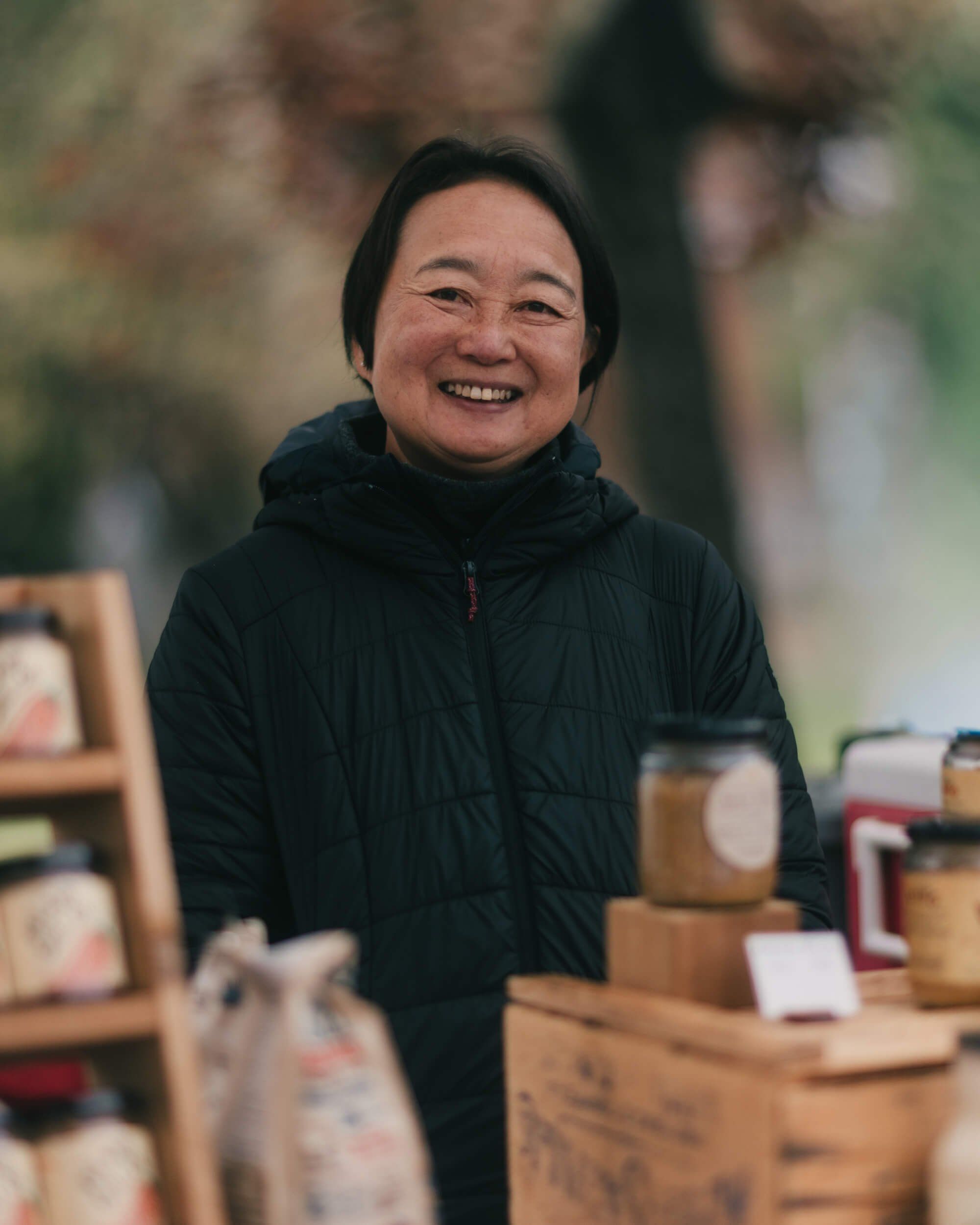Smiling vendor at outdoor market stand with wooden display boxes and soft natural light
