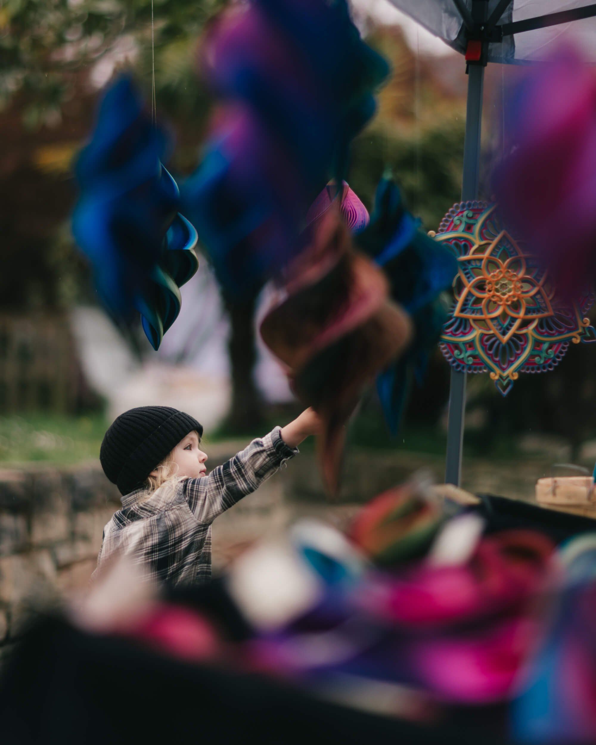 Child reaching toward vibrant blue and pink street art installation at outdoor market, soft natural light