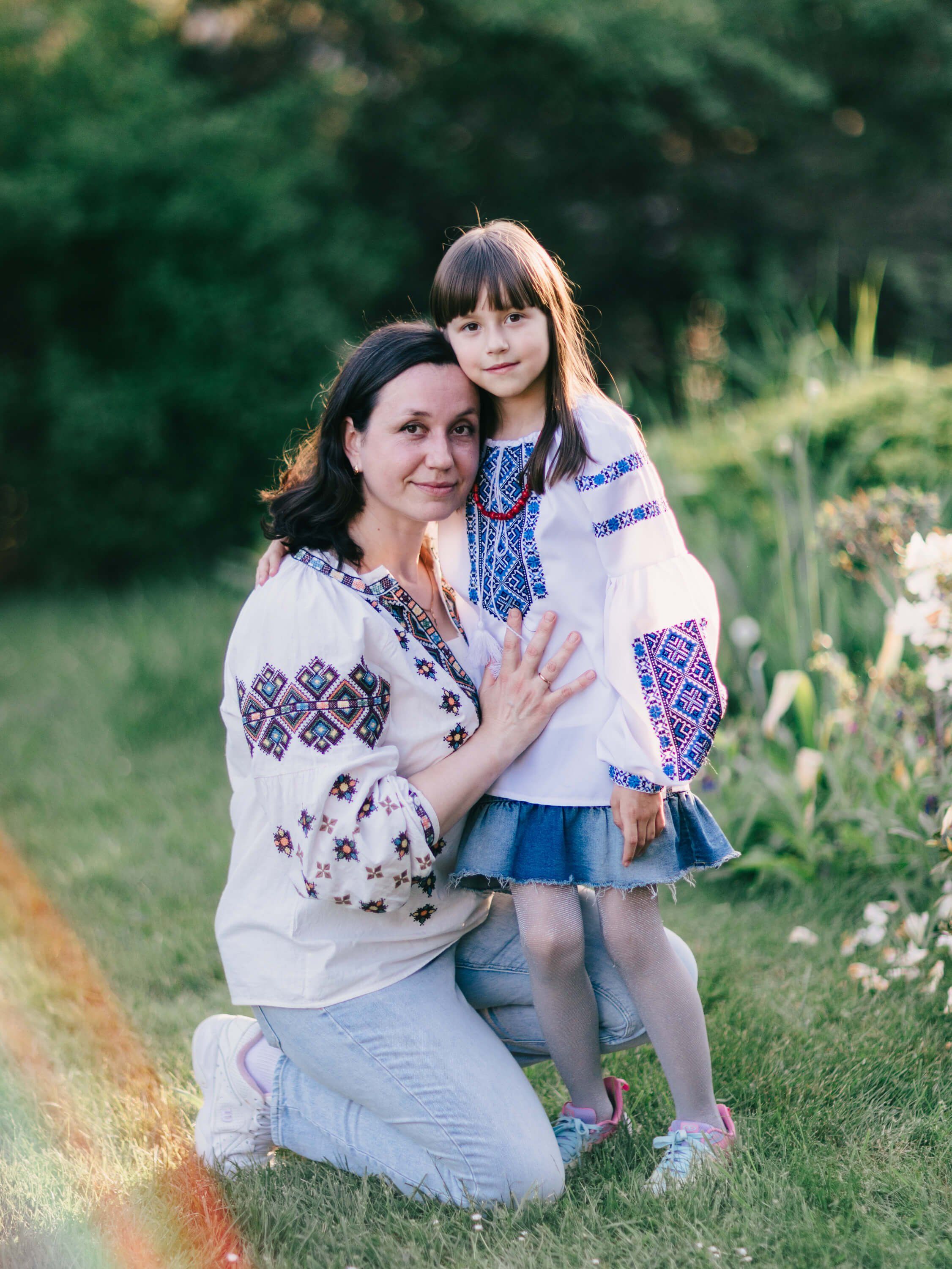 Woman and girl wearing embroidered Ukrainian vyshyvanka smiling together in golden-hour garden light
