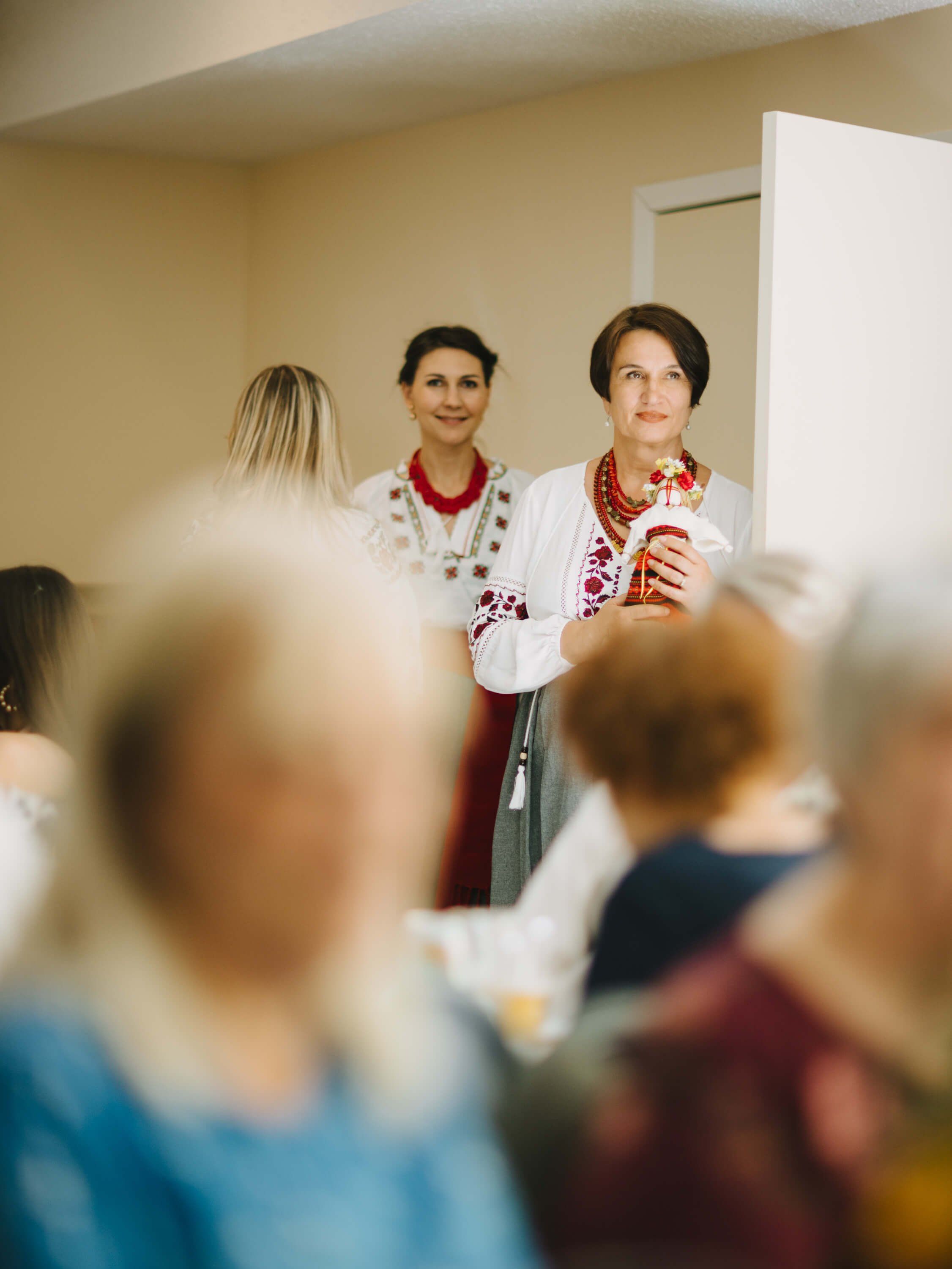 Two women in embroidered white blouses greet guests in a warm-lit room during the Ukrainian fundraiser dinner