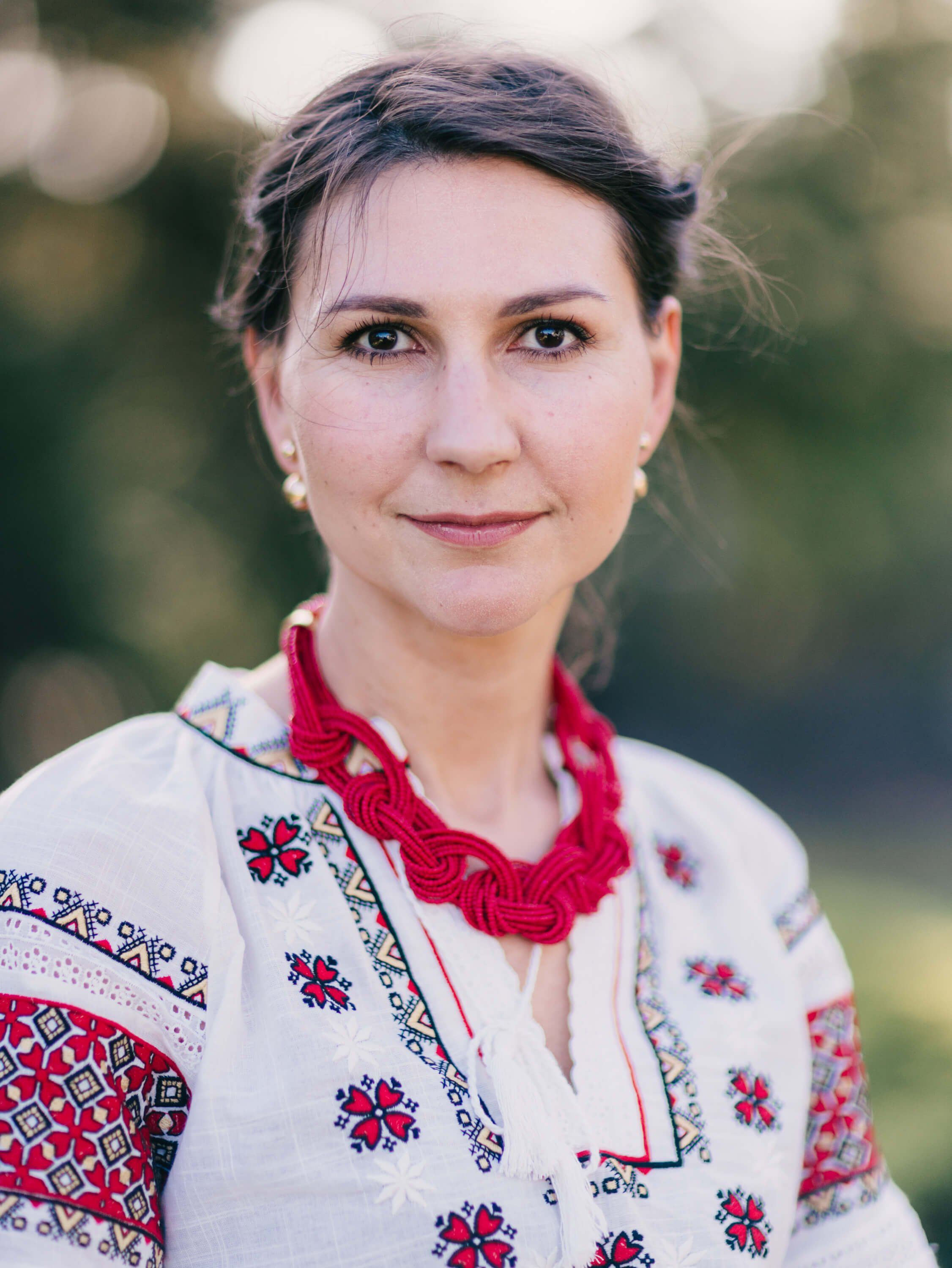 Woman in embroidered Ukrainian blouse with red crocheted collar, soft natural light, gentle outdoor setting