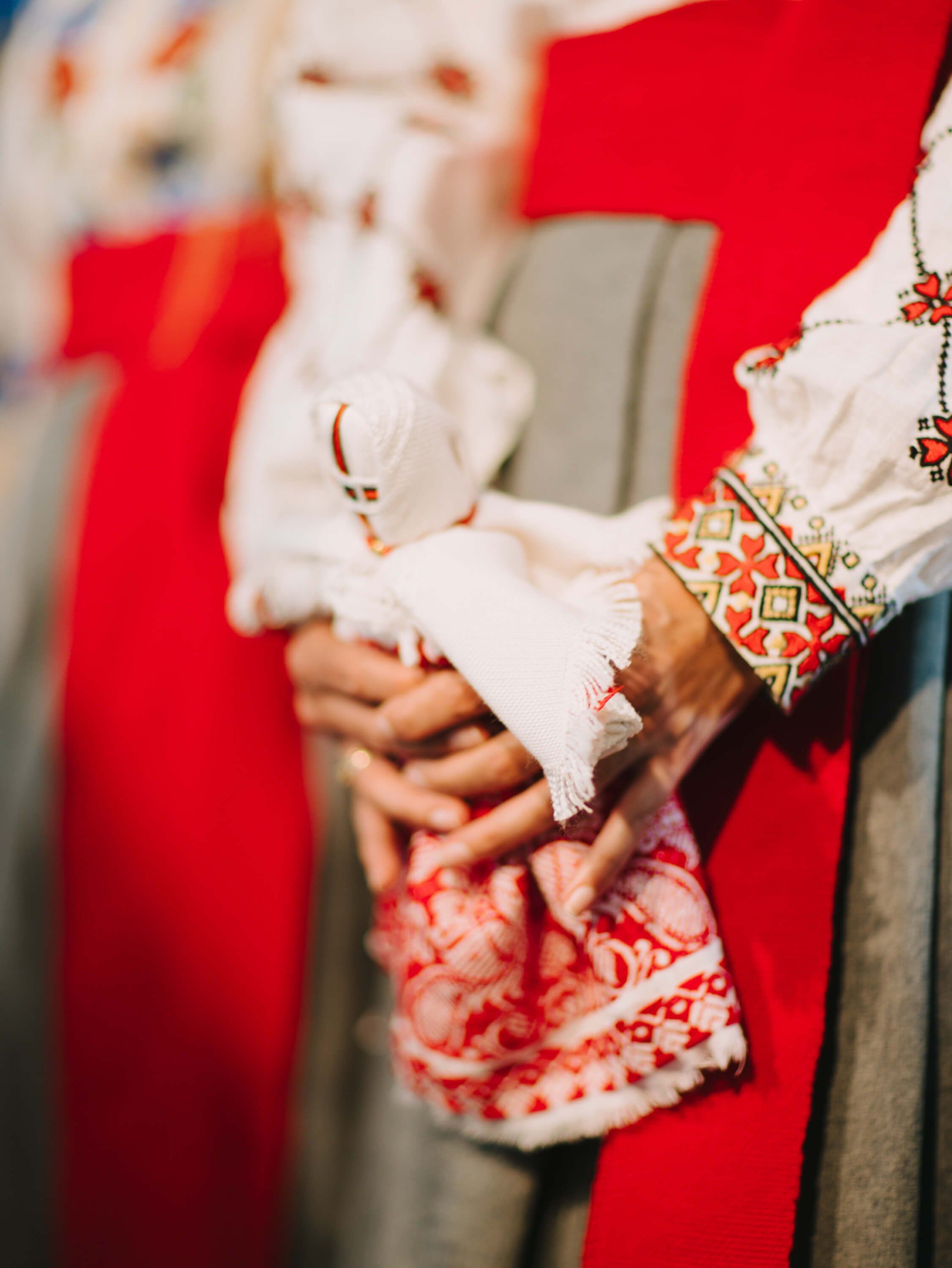 Hands clasped in traditional Ukrainian embroidered dress against red fabric, intimate moment of connection at formal event