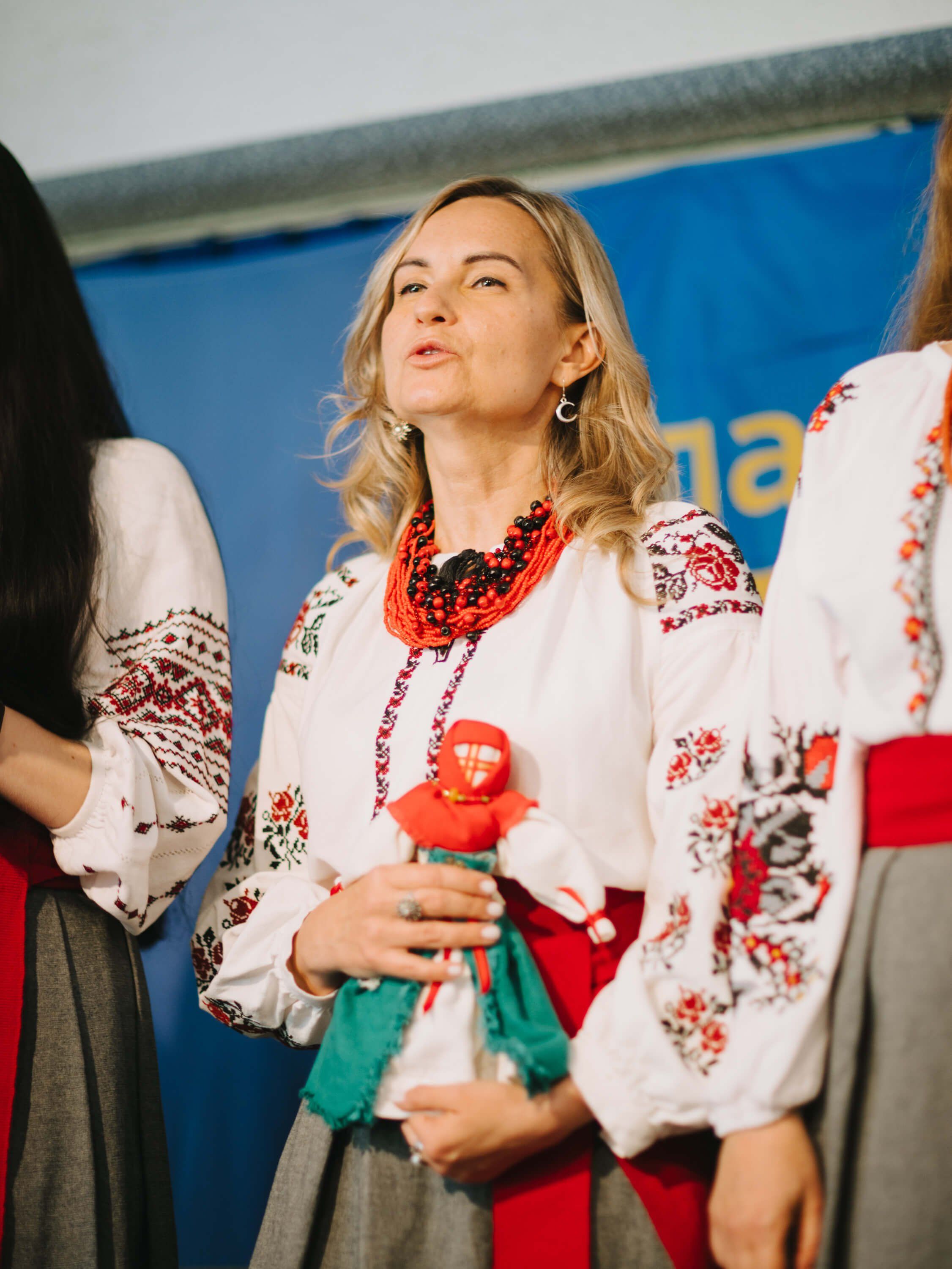 Woman in embroidered white blouse and red beaded necklace holds a decorative doll at a Ukrainian fundraiser dinner