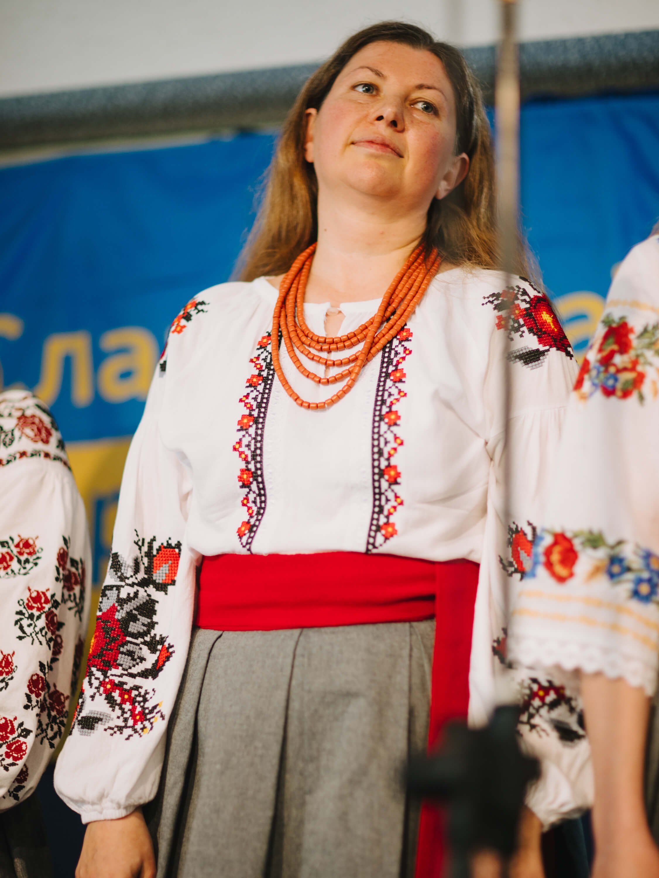 Woman in traditional Ukrainian embroidered white blouse and red skirt gazes upward during fundraiser dinner