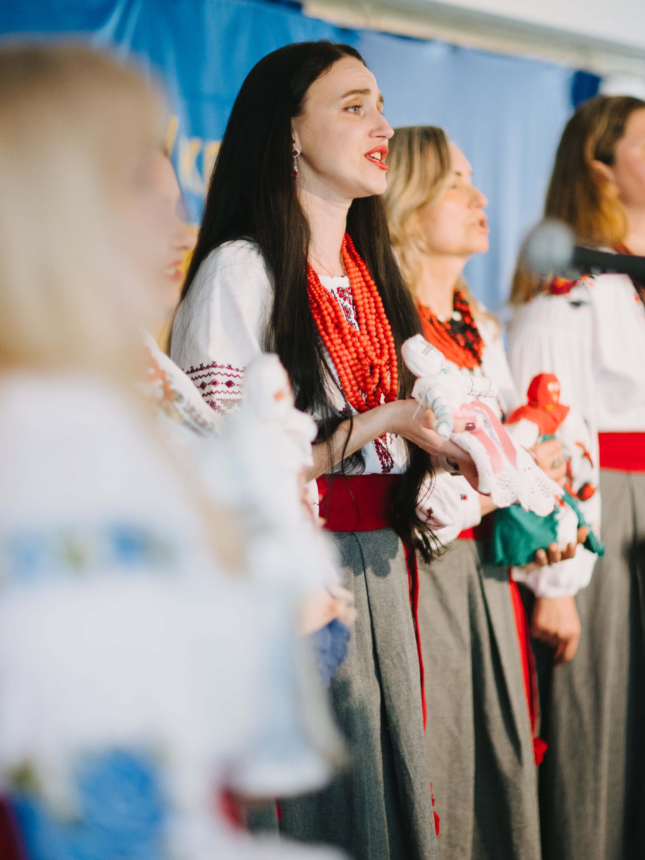 Woman in traditional Ukrainian embroidered dress and red beaded necklace stands with others at a fundraiser dinner event