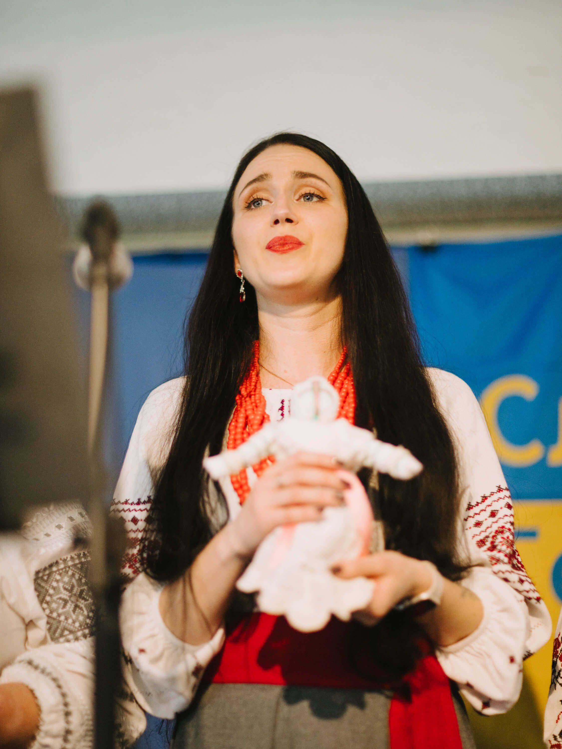 Woman in traditional Ukrainian embroidered dress holds white cloth, gazing upward at Salt Spring Island fundraiser dinner
