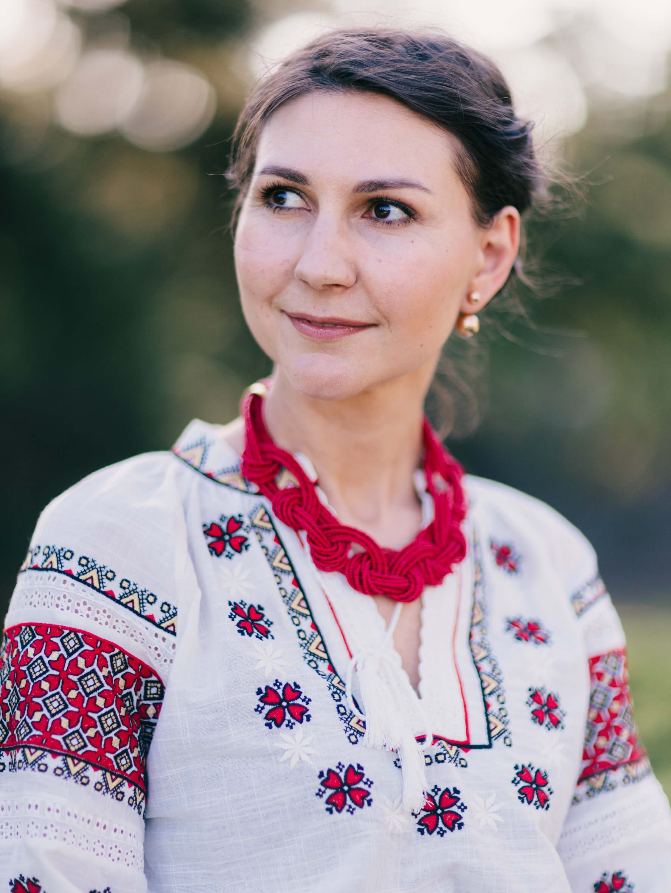 Woman in embroidered white linen shirt with red geometric patterns and crimson neckwear, soft-focused natural background, warm golden hour light
