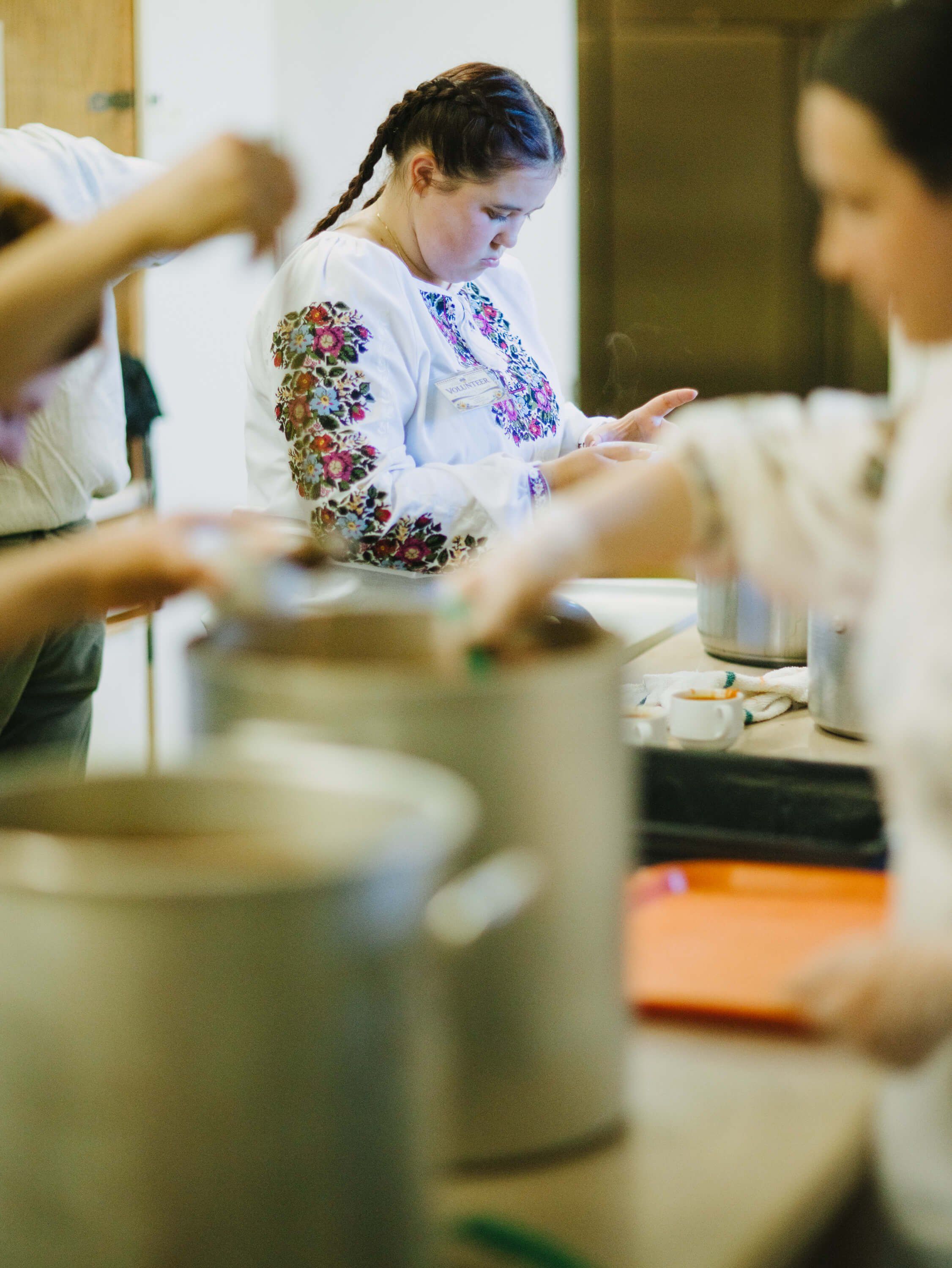 Woman in embroidered white blouse focuses intently while preparing food at a communal kitchen table during the fundraiser dinner